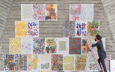 Lehrperson auf Leiter beim Aufhängen von Entwürfen in der Maurerhalle.