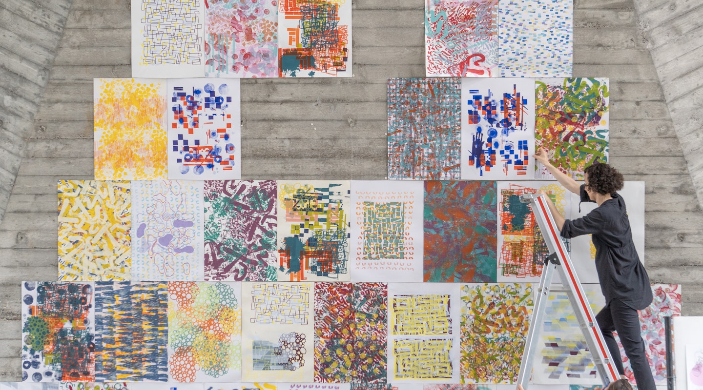 Lehrperson auf Leiter beim Aufhängen von Entwürfen in der Maurerhalle.