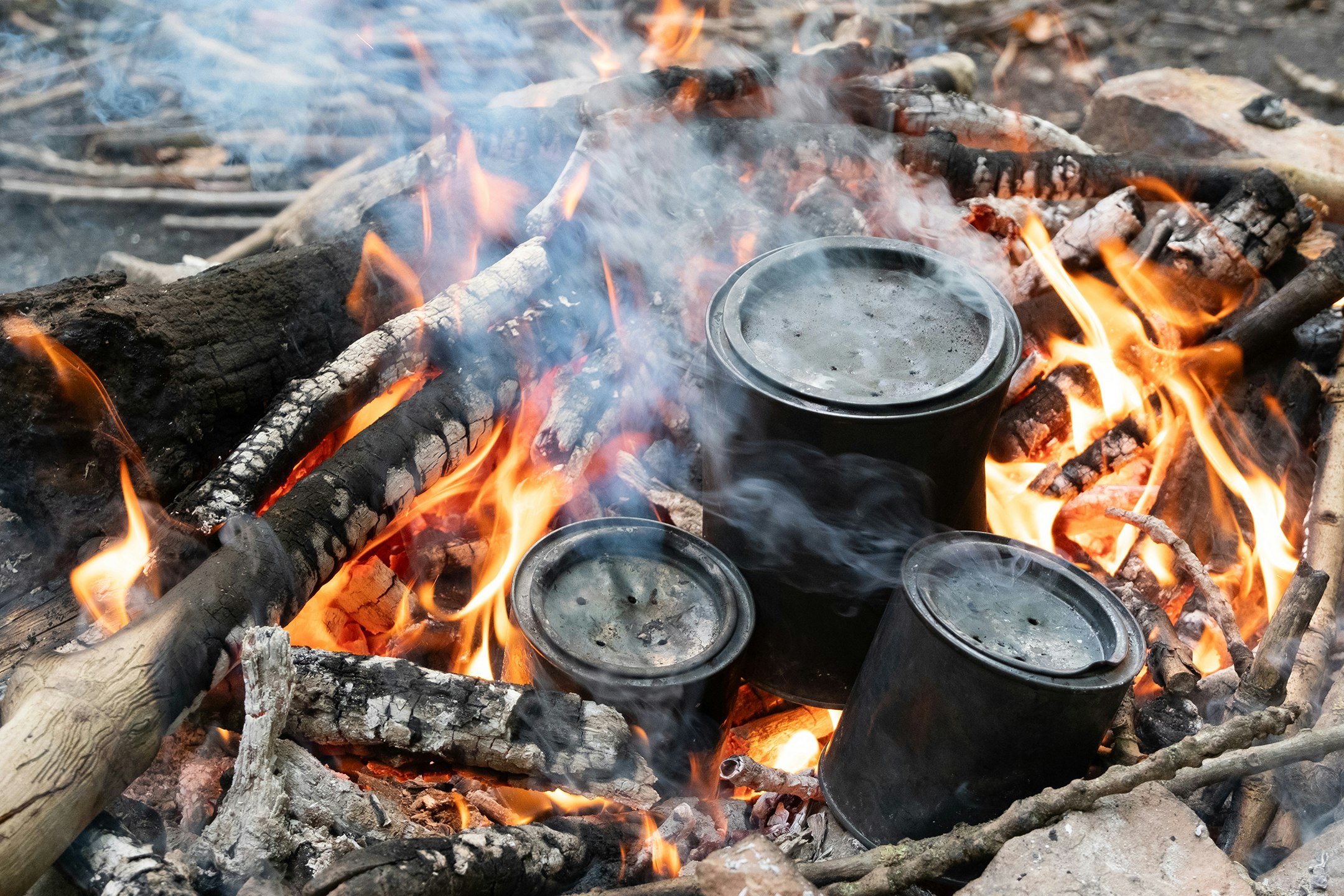 Ein Feuer brennt. Alu-Dosen sind mit einem Deckel verschlossen und ganz schwarz. Sie stehen in der Glut. Im Feuer. Rings herum brennt das Feuer.