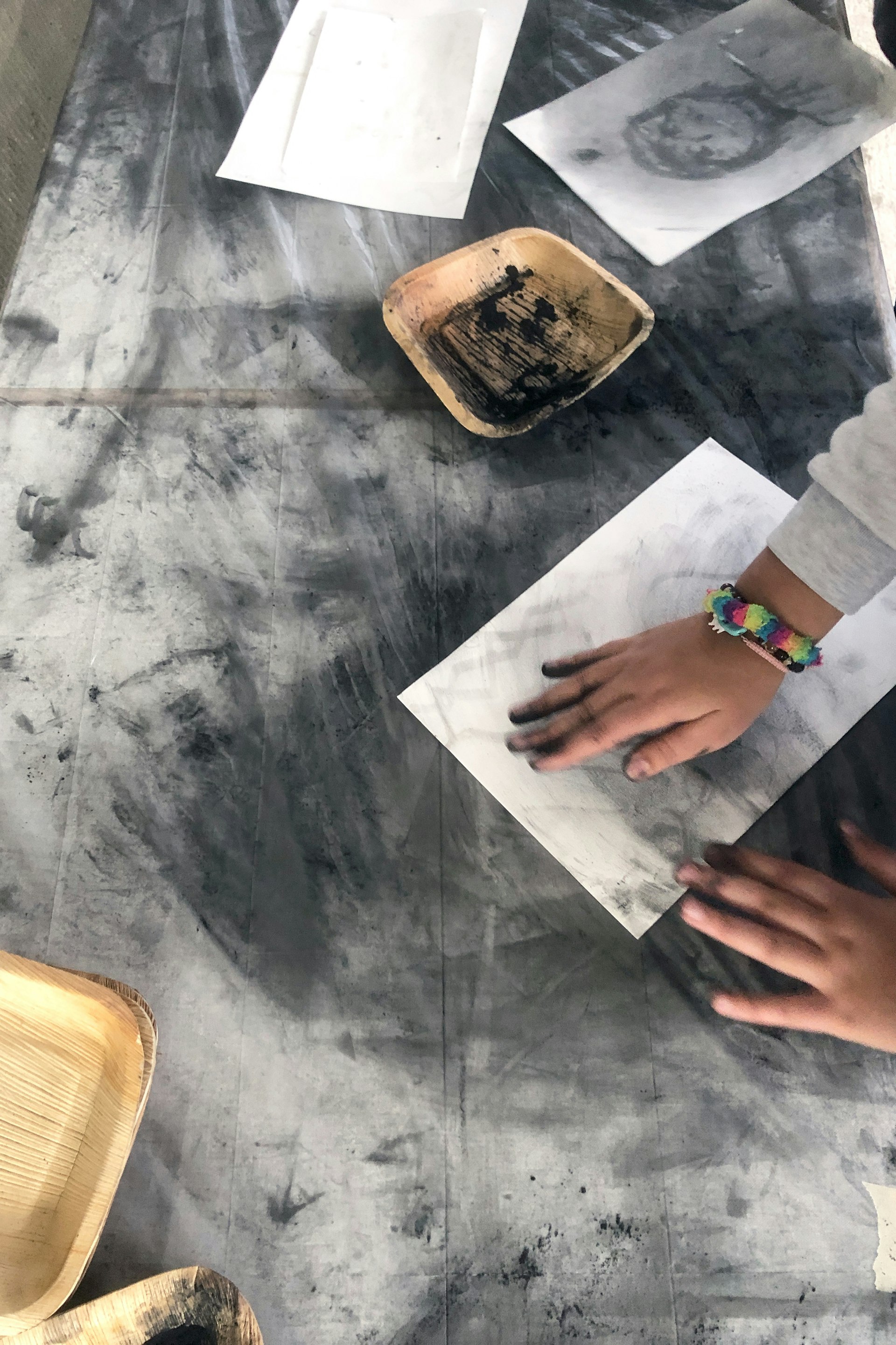 Kinderhände, vor ihm liegt eine Skizzen mit Zeichenpapier. Es zeichnet mit seinen Fingern und zerreibt das Kohelpulver auf dem Papier.