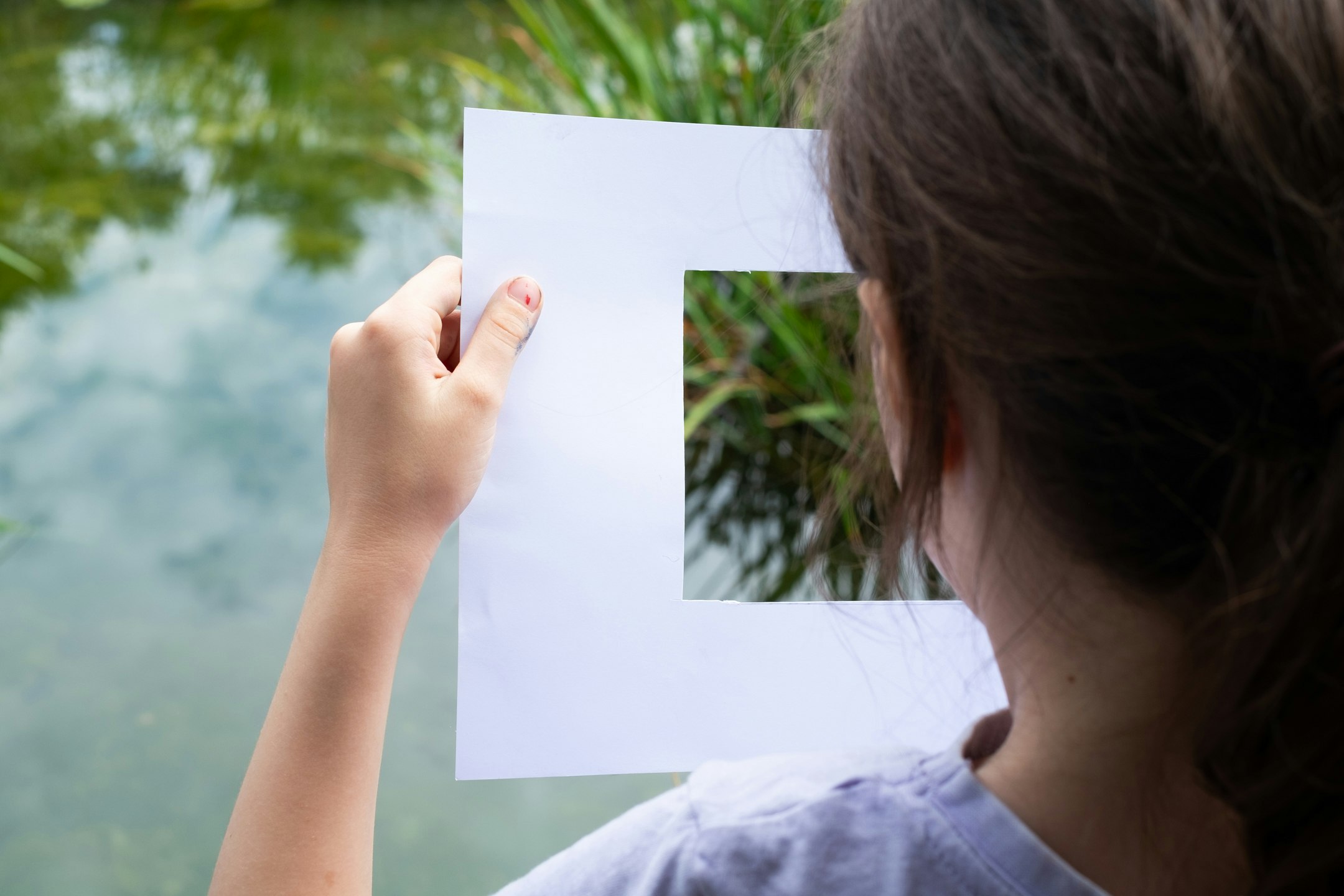 Kind schaut durch rechteckige Schablone, von hinten zu,  Teich hinten