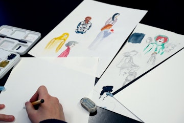 Eine Person zeichnet und malt skizzenhaft verschiedene Figuren auf Papier.