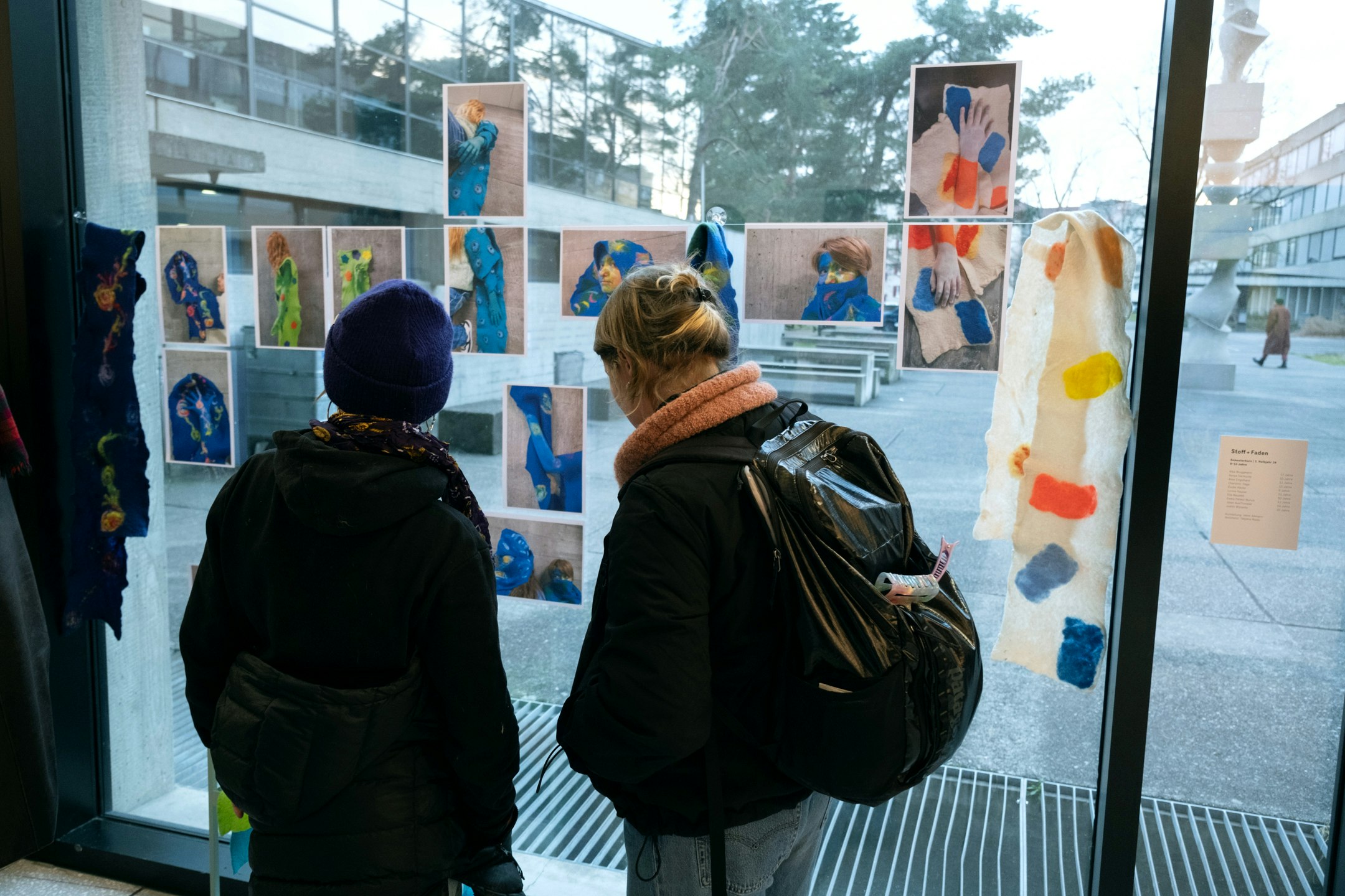 Fotos und selbst gefilzete Schals sind an einer grossen Fensterscheibe ausgestellt.
