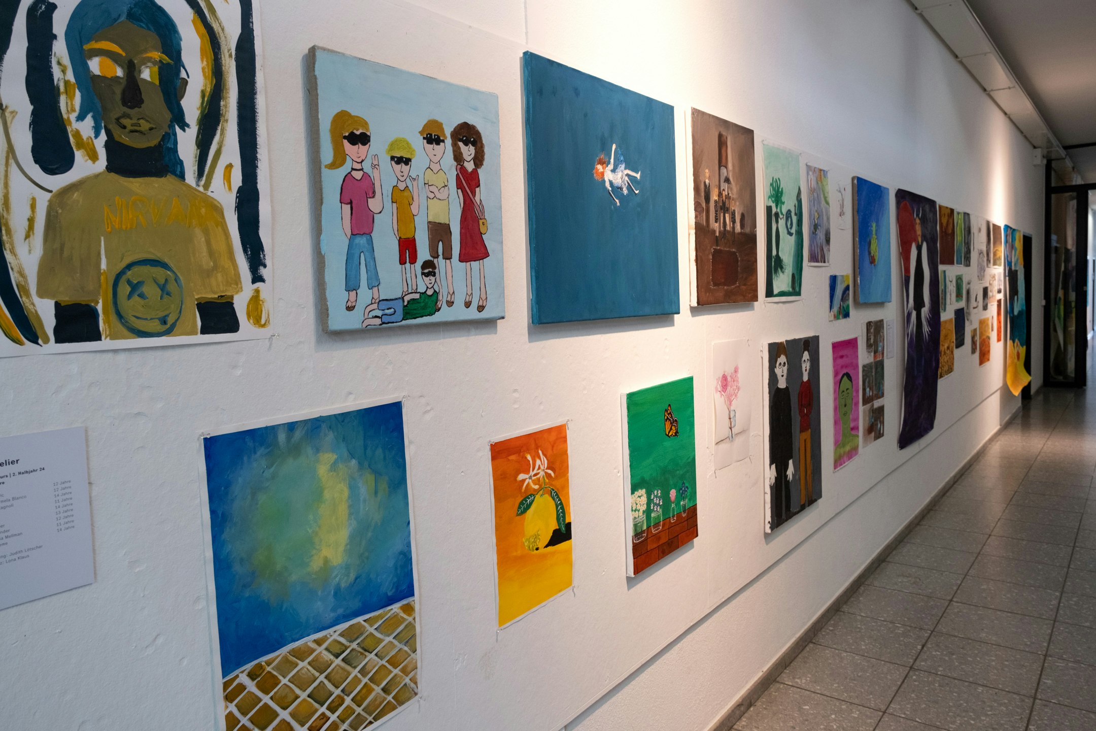 Malereien von Kindern und Jugendlichen auf Papier und Leinwänden an einer Wand