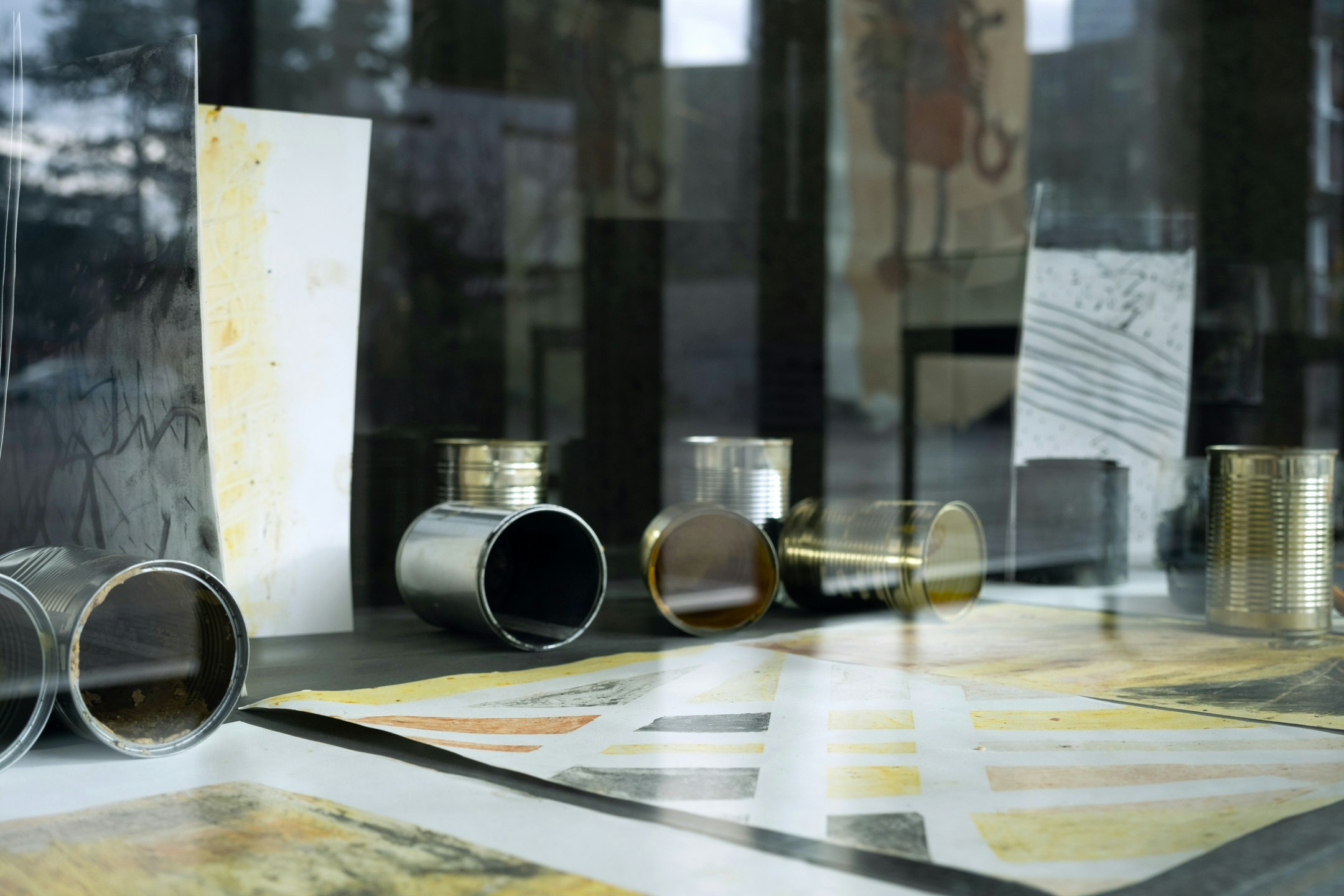 Wachsmalbilder und Kohlezeichnungen, Aludosen und selbsthergestellte Wachsmalstifte sind einer einer Vitrine ausgestellt.