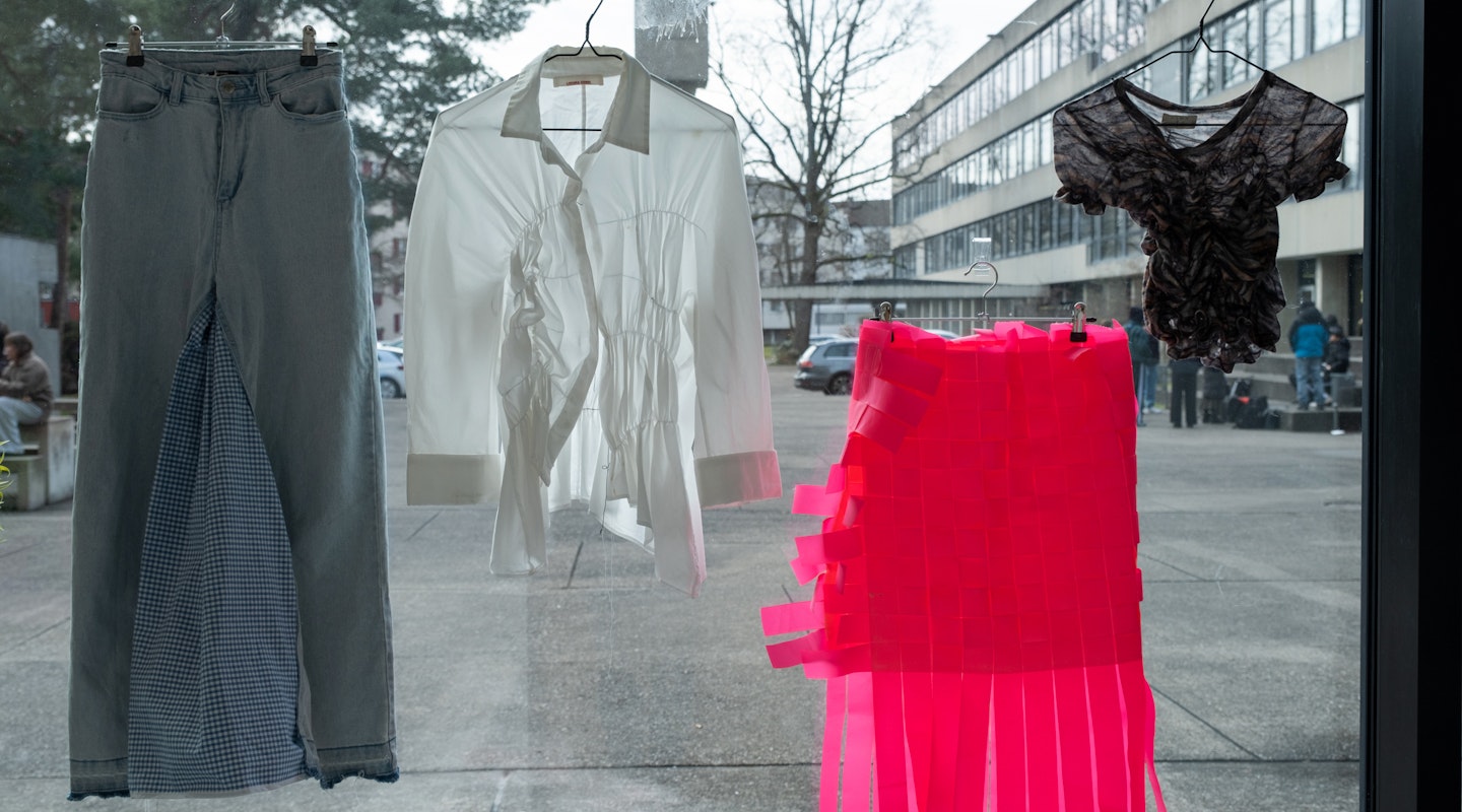 Von Kindern hergestellte Stoffobjekte und Kleidungsstücke sind an einer Fensterscheibe der Schule für Gestaltung Basel ausgestellt.