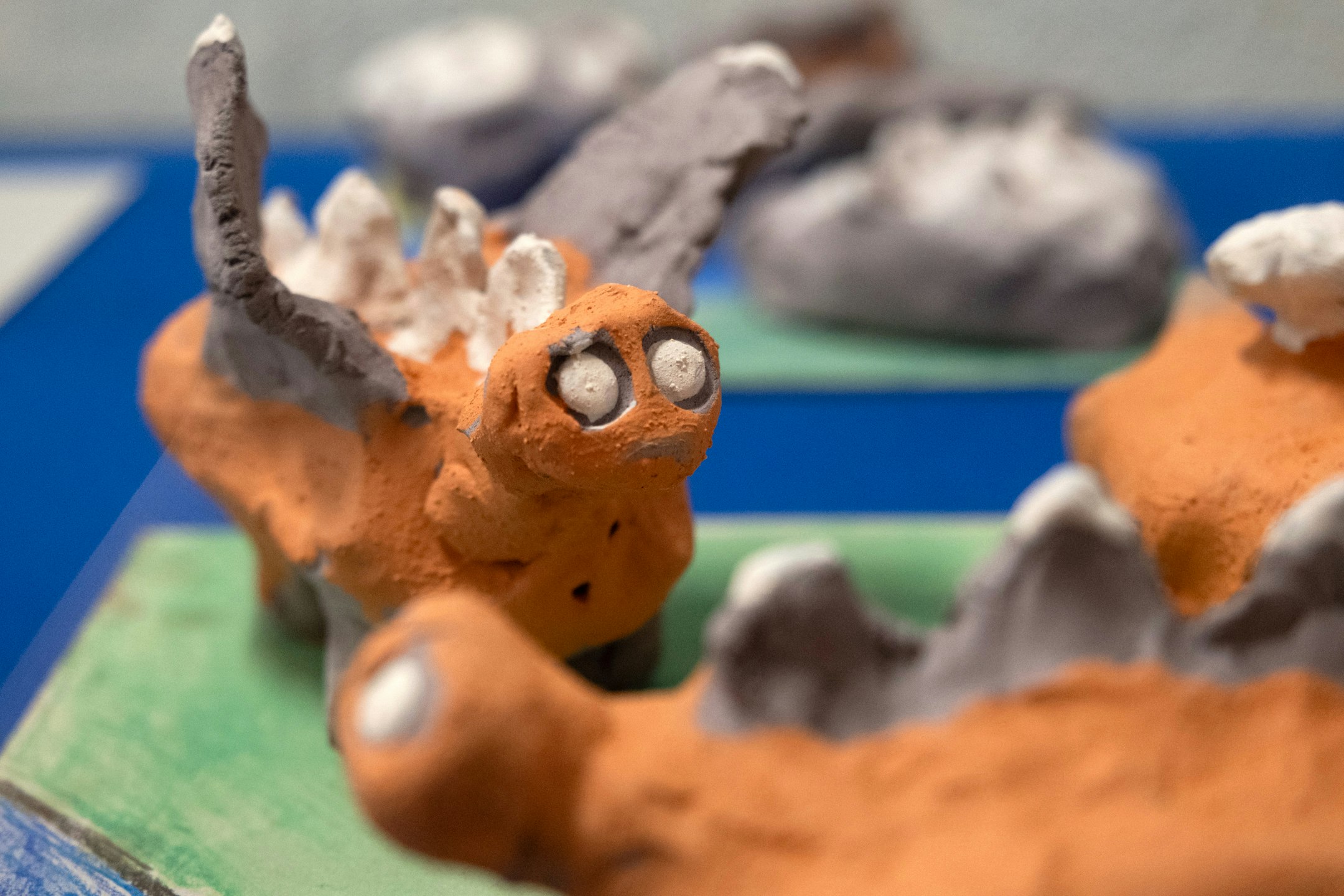 Von Kindern aus Ton modellierte Fabelwesen sind in einer Vitringe ausgestellt. Die Fabelwese sind mit Engoben bemalt. Sie liegen auf bemalten Kartons.