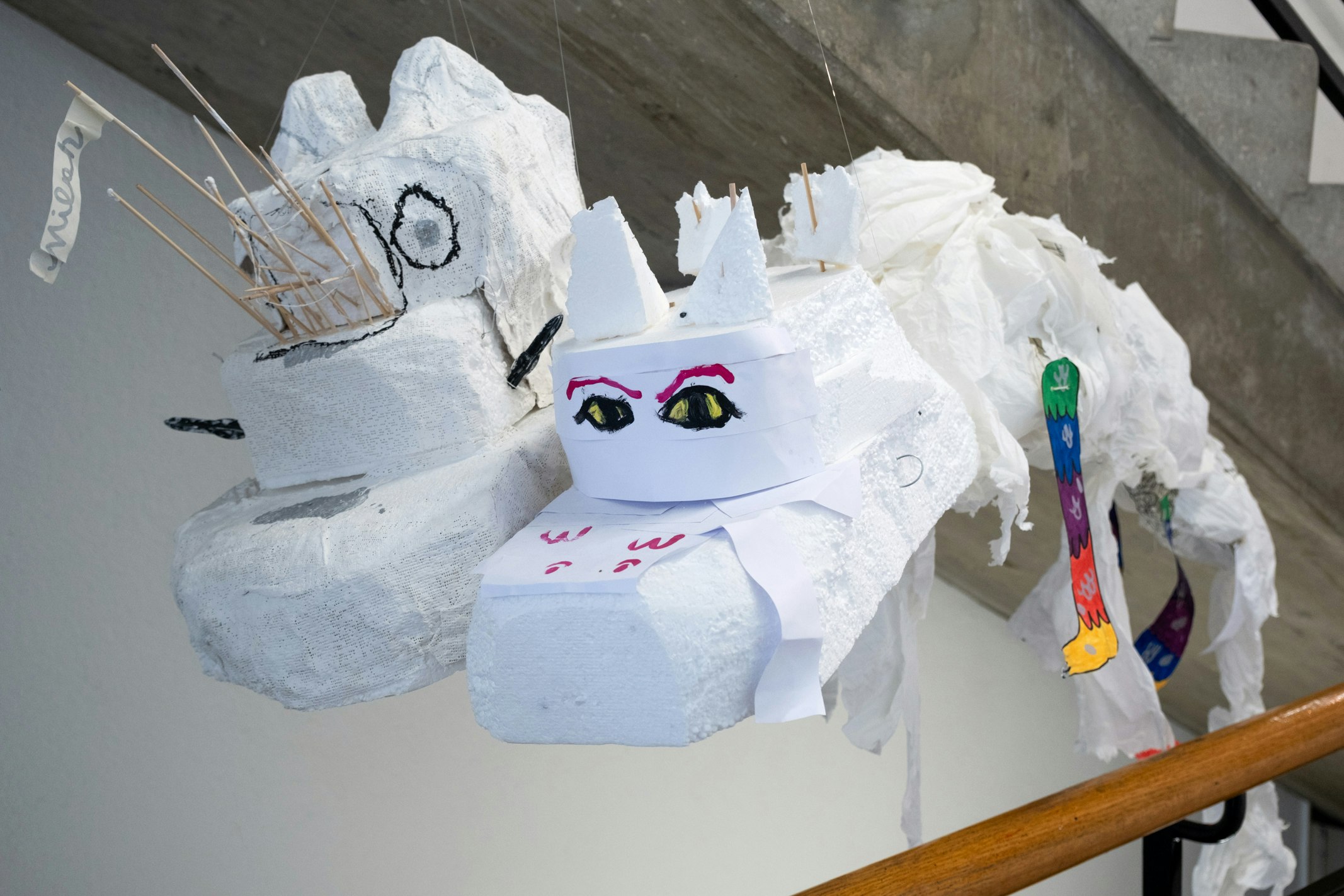 Flugobjekte aus Gips, Weidengeflecht, Schnur, Papier, Karton und Klebeband sind auf einem Geländer und an Schnur an der Decke befestigt. Die Objekte sind von Kindern gemacht.