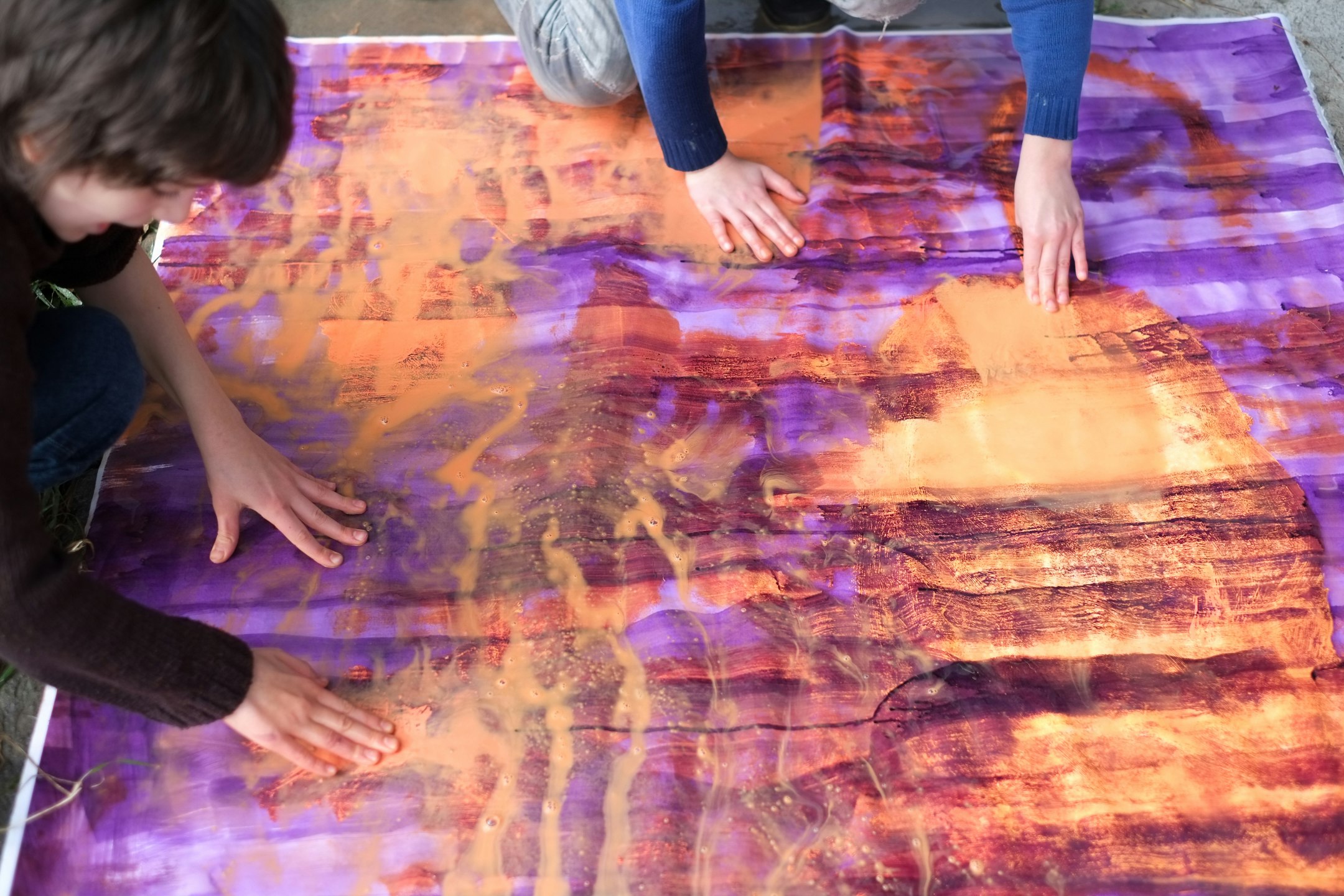 Papier am Boden, farbig bemalt, Kinder zerreiben die Farbe