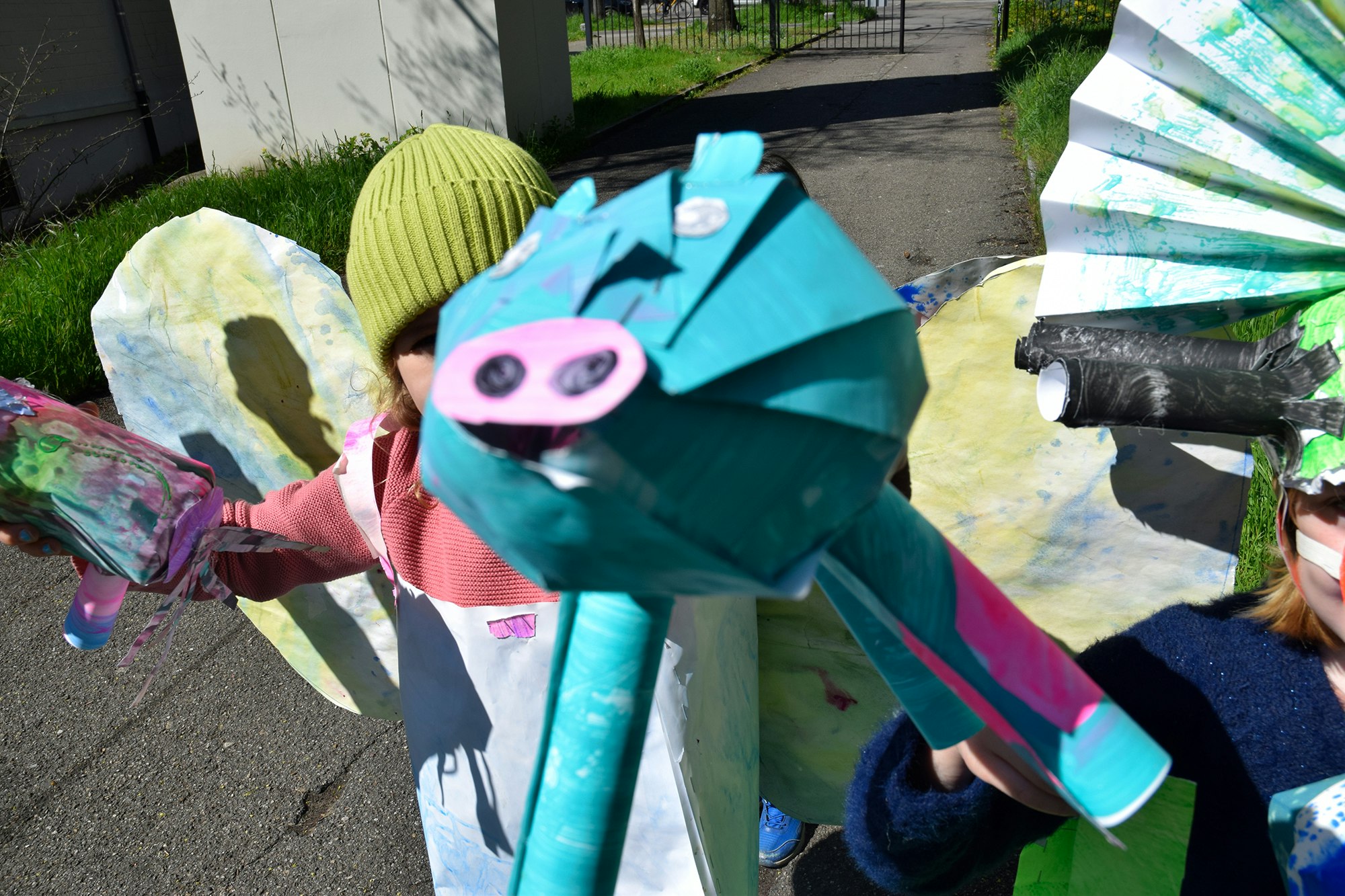 Zwei Kinder tragen Masken aus Papier. Die Masken sind bemalt. In ihren Händen tragen sie Tierfiguren, die ebenfalls bemalt sind.