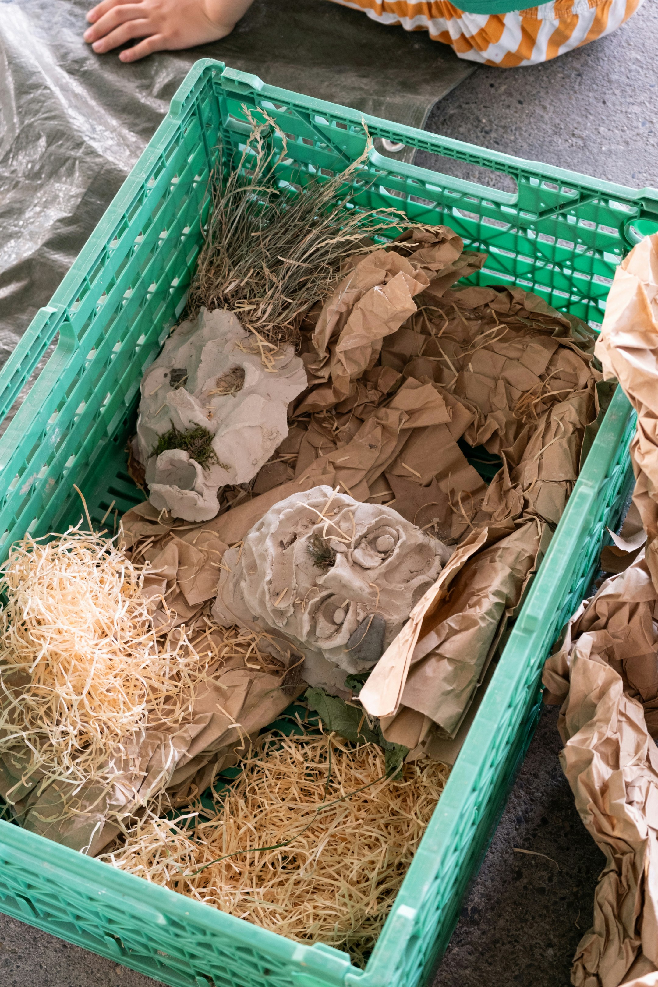 Tonfiguren liegen in einer Plastikkiste. Sie sind gepolstert mit Holzwolle.