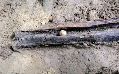 Eine Lehmkugel liegt in einer Holzrinde. Der Boden ringsherum ist lehmig.