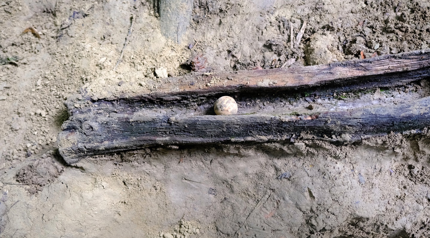 Eine Lehmkugel liegt in einer Holzrinde. Der Boden ringsherum ist lehmig.