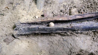 Eine Lehmkugel liegt in einer Holzrinde. Der Boden ringsherum ist lehmig.