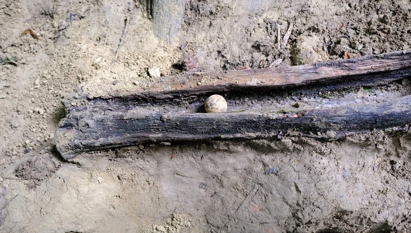 Eine Lehmkugel liegt in einer Holzrinde. Der Boden ringsherum ist lehmig.