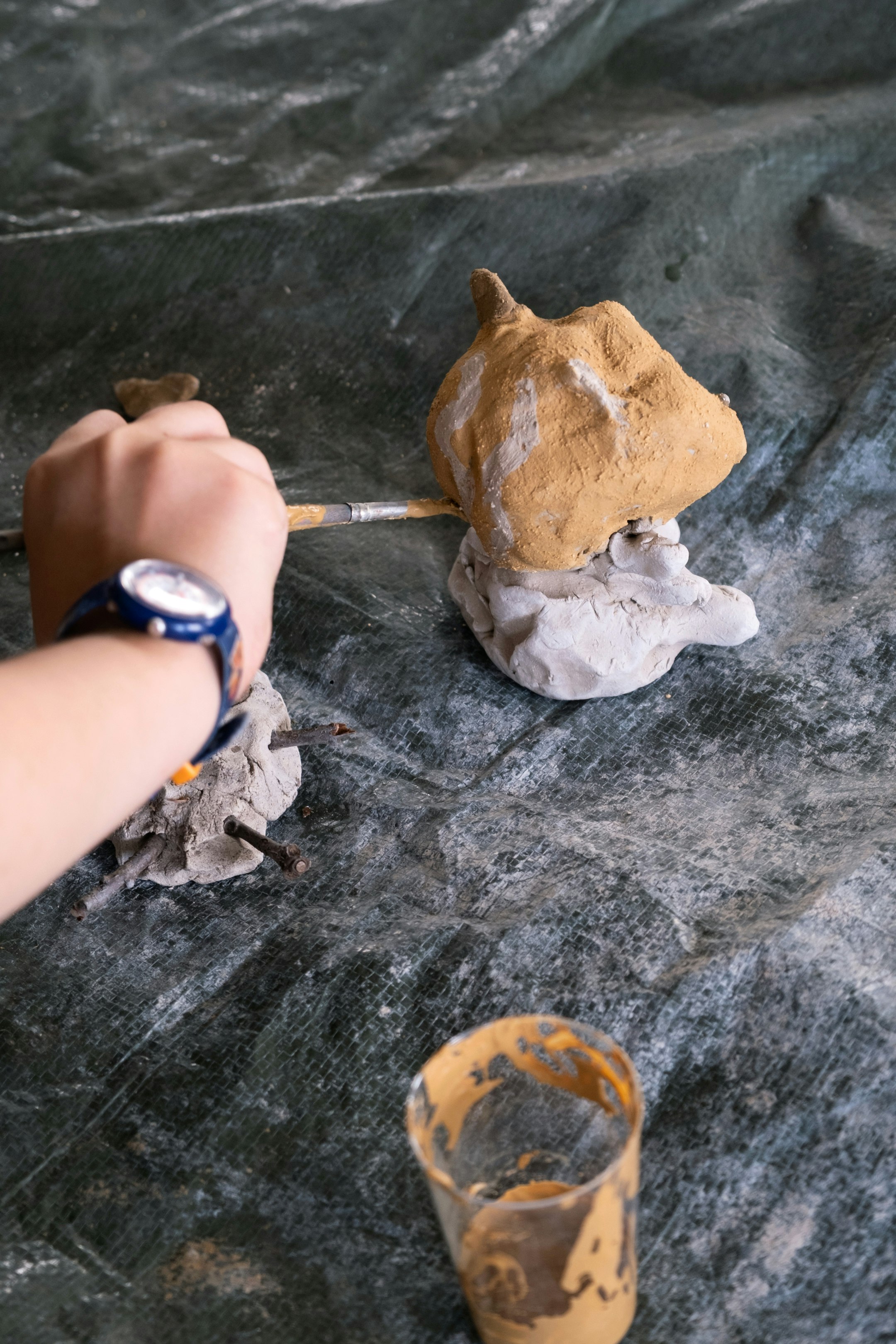 Ein Kind bemalt eine Tonfigur. DIe Tonfigur steht auf einer Blache.