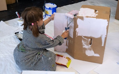 Ein Kind sitzt auf dem Boden und bemalt eine Kartonschachtel.