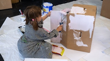 Ein Kind sitzt auf dem Boden und bemalt eine Kartonschachtel.