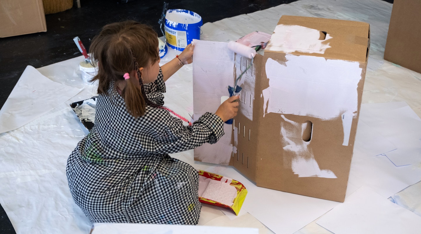 Ein Kind sitzt auf dem Boden und bemalt eine Kartonschachtel.