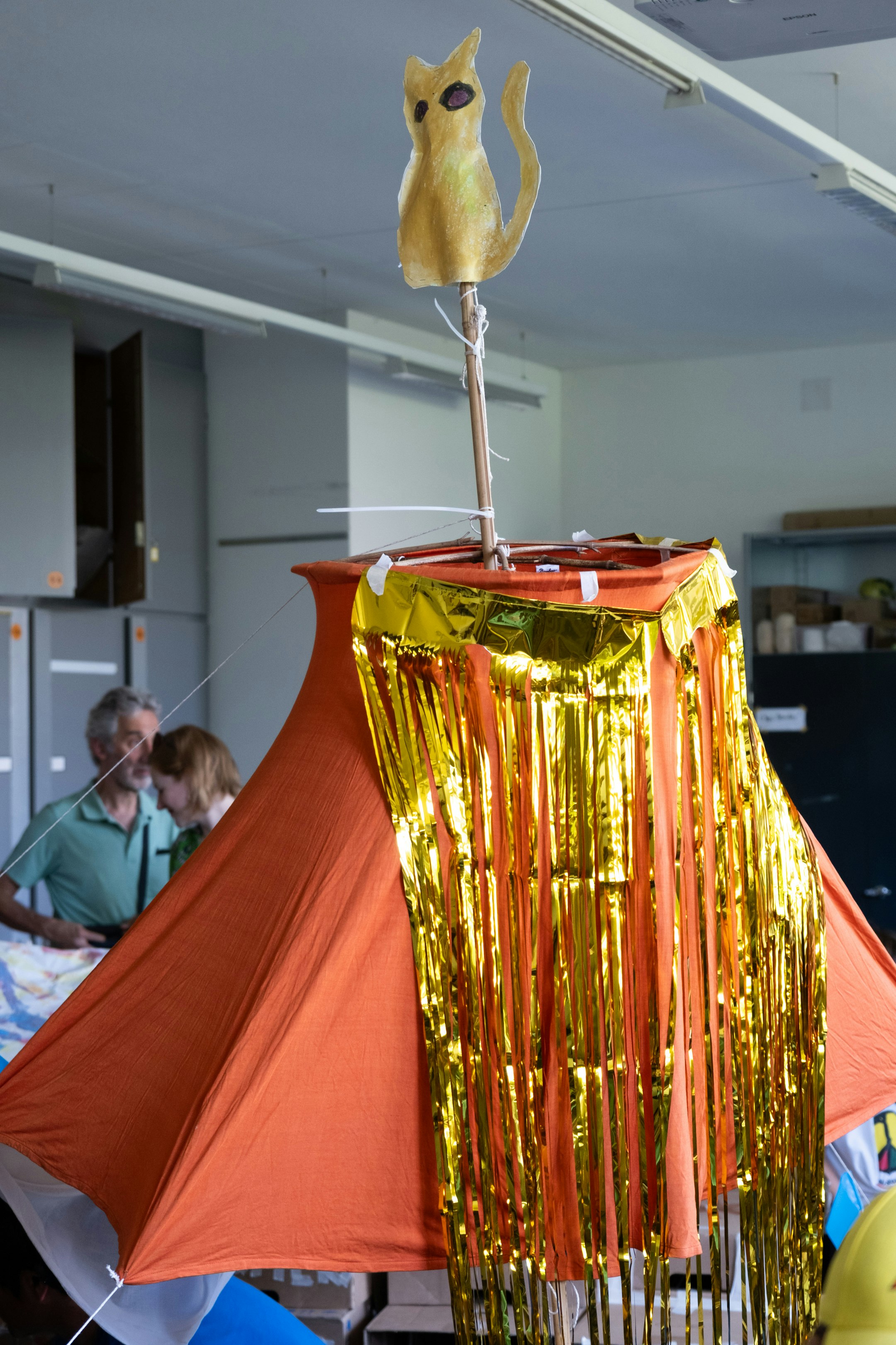 Installation aus verschiedenen Materialien in einem Raum. Im Hintergrund sind zwei erwachsene Menschen sichtbar.