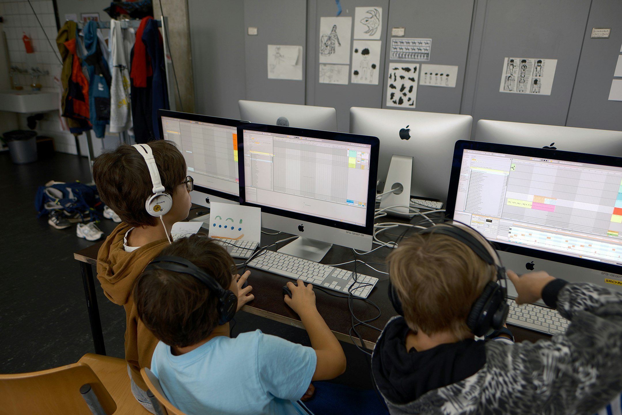 Kinder sitzen vor einem Computer und arbeiten daran. Sie tragen Kopfhörer.