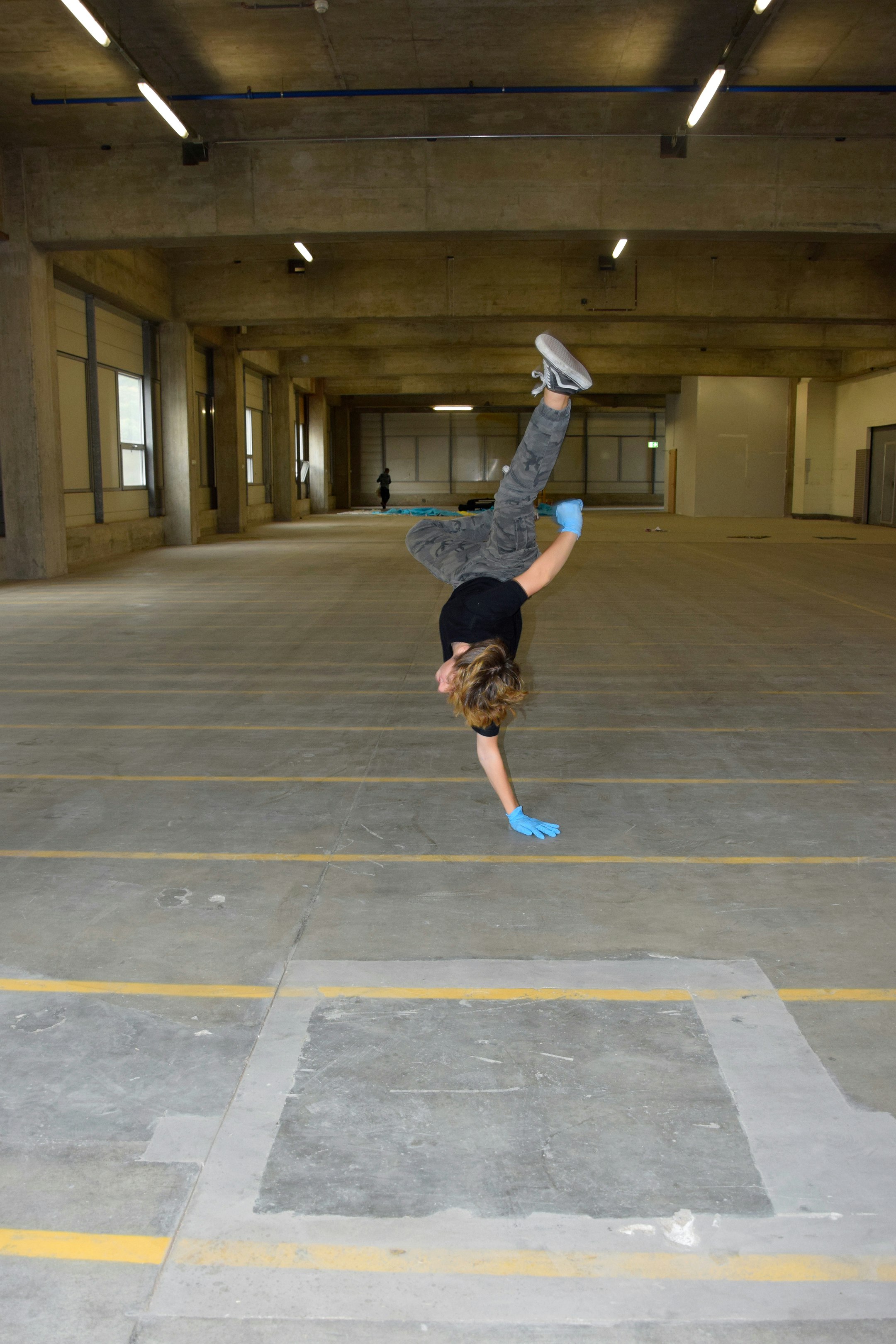 Eine jugendliche Person tanzt in einer leeren Fabrikhalle.