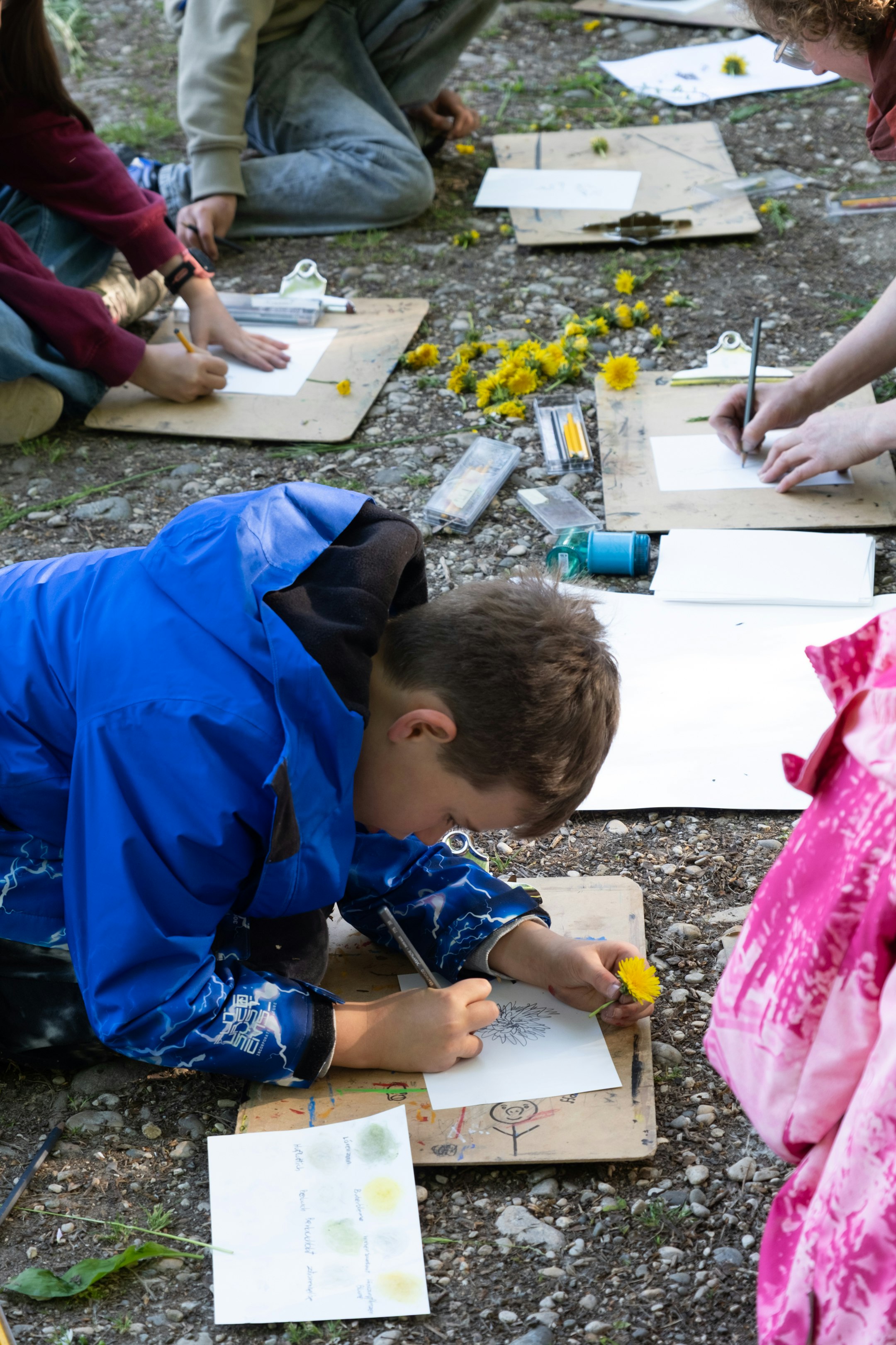 Kinder und eine Lehrperson, die draussen Blumen abzeichnen