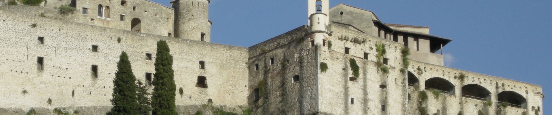 Il Castello di Itri si erge maestoso contro un cielo azzurro, con antiche mura in pietra e torri storiche circondate da vegetazione rigogliosa.