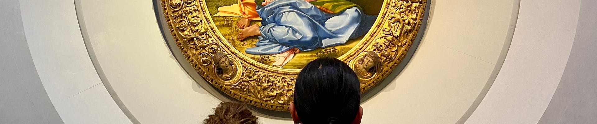 Festa dei Doni 31.01.2024 Due persone osservano un dipinto circolare in un museo, circondato da una cornice decorativa intricata e appeso su una parete grigia.