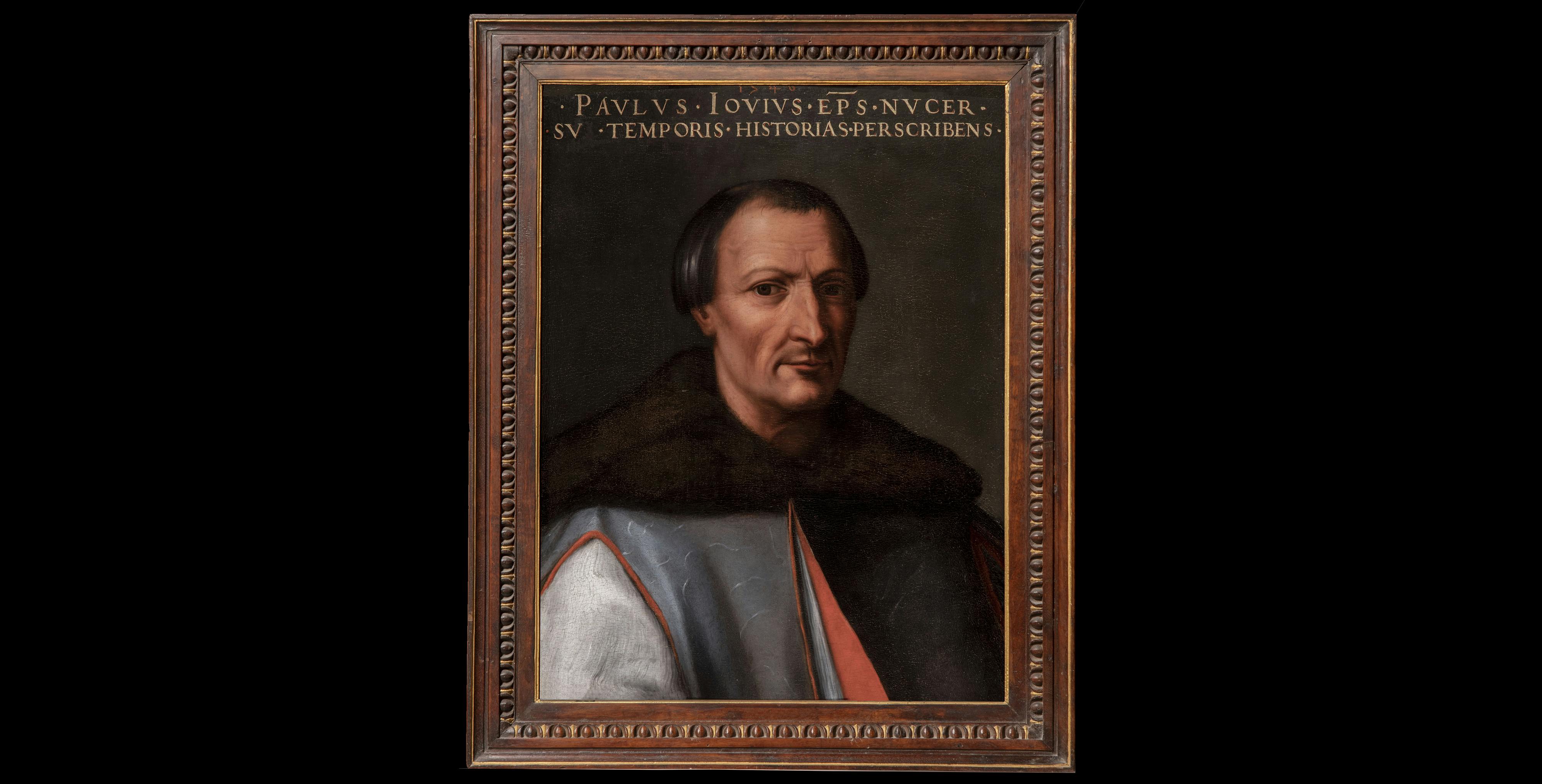 Un ritratto storico di un uomo in abiti rinascimentali, con un'espressione seria, incorniciato in una cornice di legno elaborata con un'iscrizione in alto, contro uno sfondo nero.