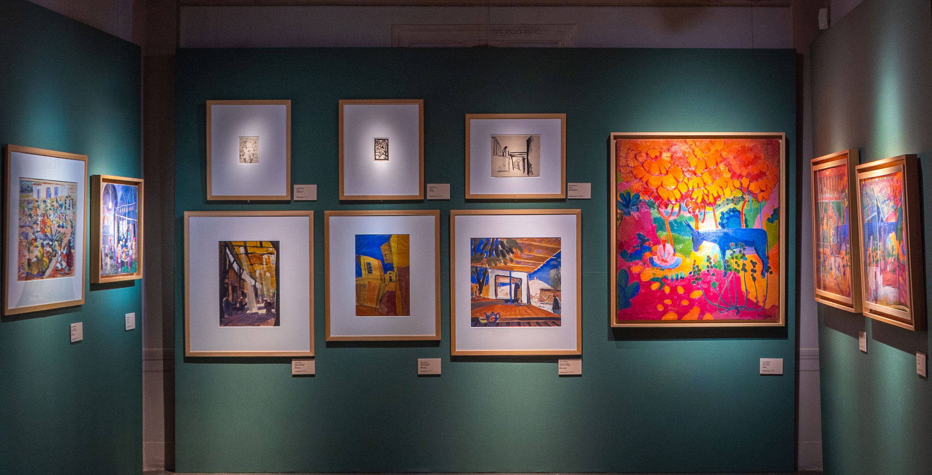 An art gallery with teal walls showcases a variety of framed paintings, including vibrant abstract and impressionist pieces, under soft lighting.