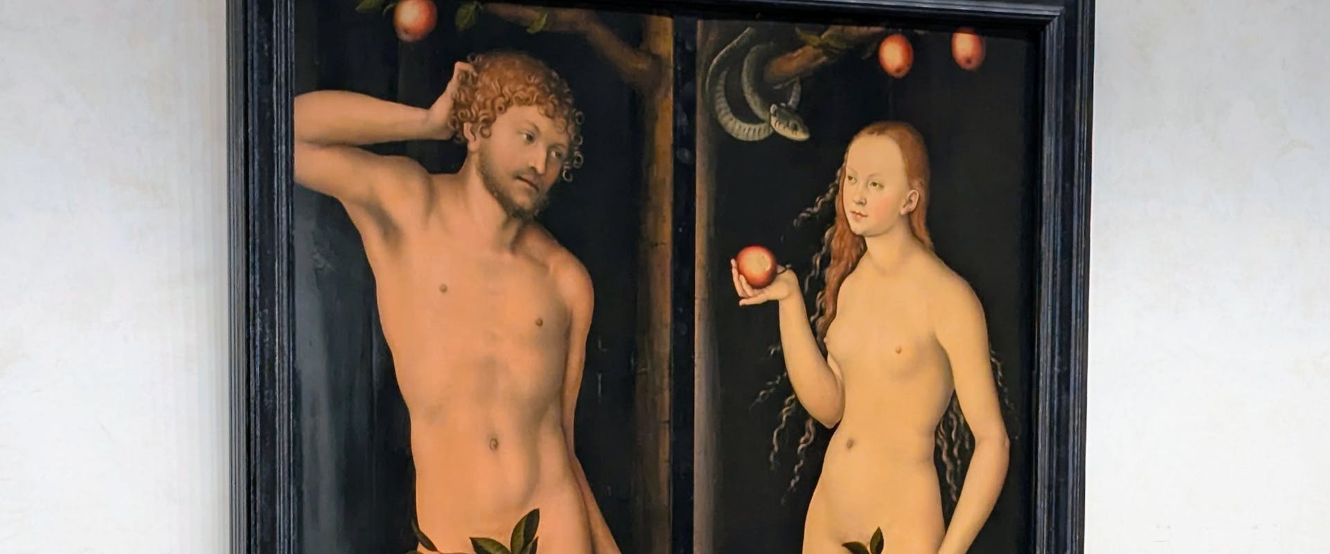 A classical painting depicts two naked figures, a man and a woman, standing on either side of a tree laden with red apples, with a serpent coiled above, set within an ornate dark frame.