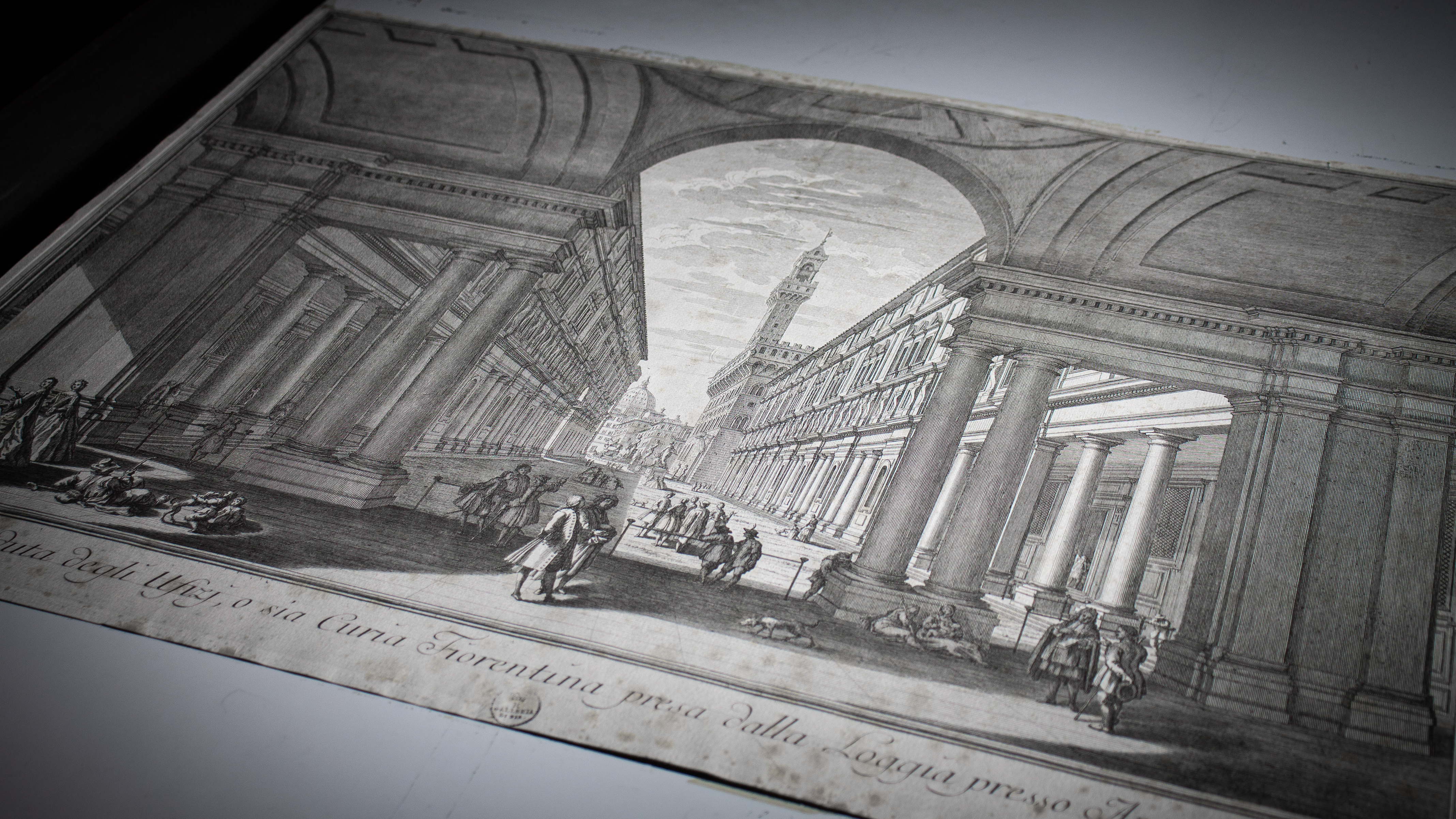 L'incisione d'epoca raffigura un imponente colonnato con archi, con una torre distante che si staglia sullo sfondo di un cielo nuvoloso, mentre figure in abiti storici animano la scena, evocando un'atmosfera rinascimentale.