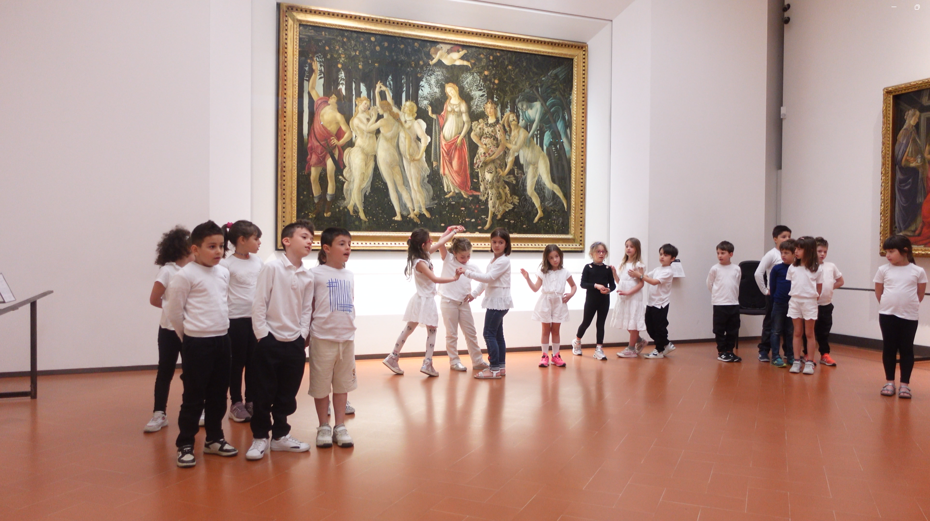 Nel museo, un gruppo di bambini in magliette bianche e pantaloni scuri è disposto in due file di fronte a un grande dipinto rinascimentale appeso alla parete, creando un contrasto tra arte classica e presenza moderna.