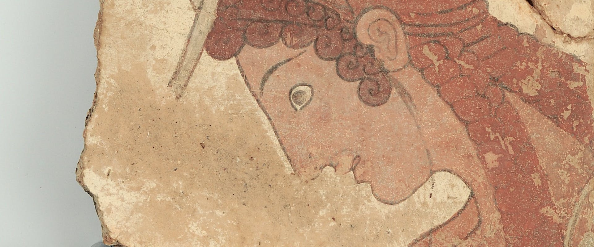 Frammento di lastra di terracotta dipinta con giovane in abiti da viaggio (ca. 500 a.C.) temporaneamente esposta al Museo Archeologico Nazionale di Firenze. Frammento di pittura murale antica con figura umana e dettagli rossi e ocra, raffigurante una persona di profilo con ornamenti sul capo.