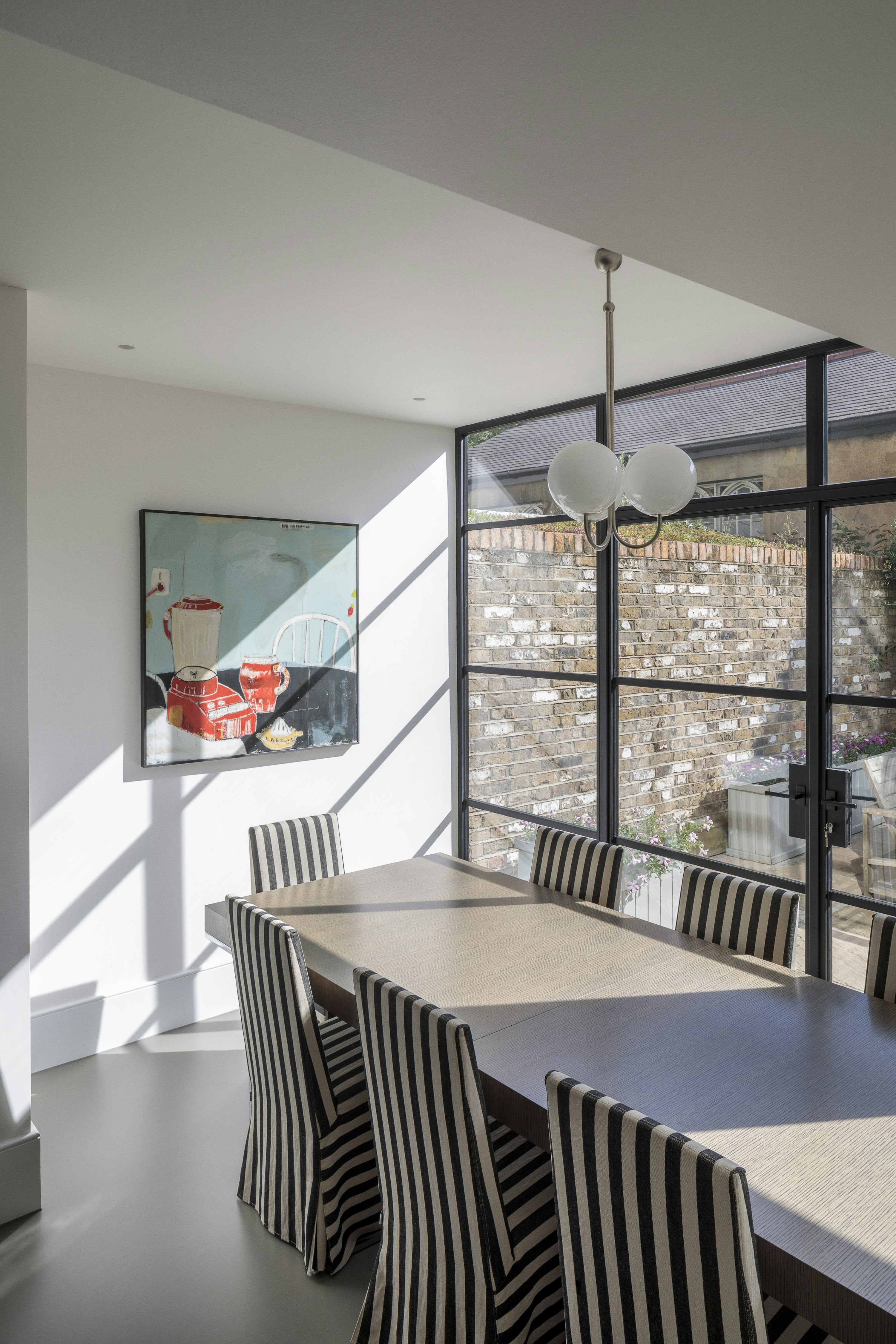 An eclectic dining room links to the garden with crittal doors, with a wooden table, striped fabric chairs and pendant light.