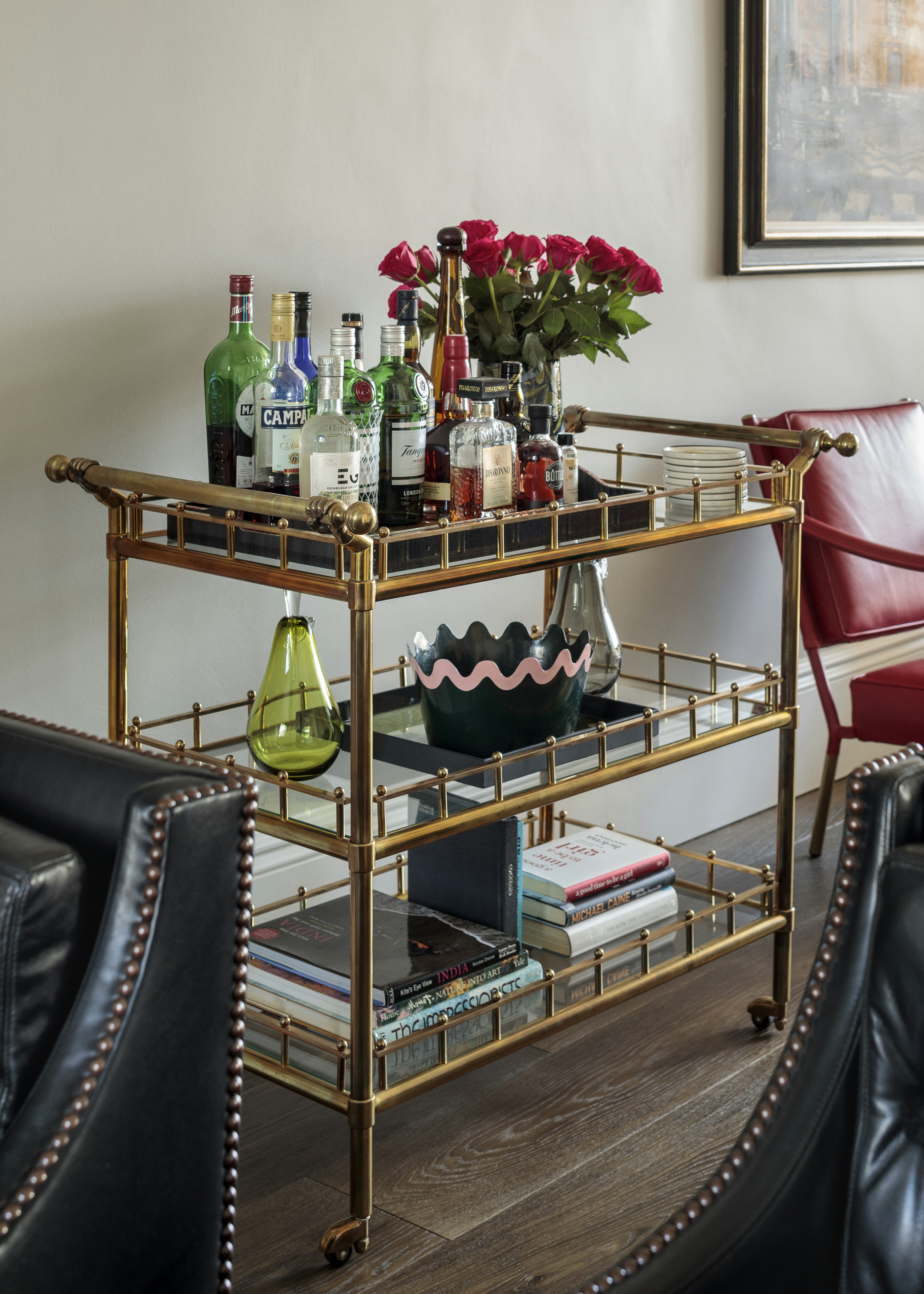 Bottles, books and flowers sit on an antique brass drinks car, in front of light-coloured walls and on dark wooden flooring.