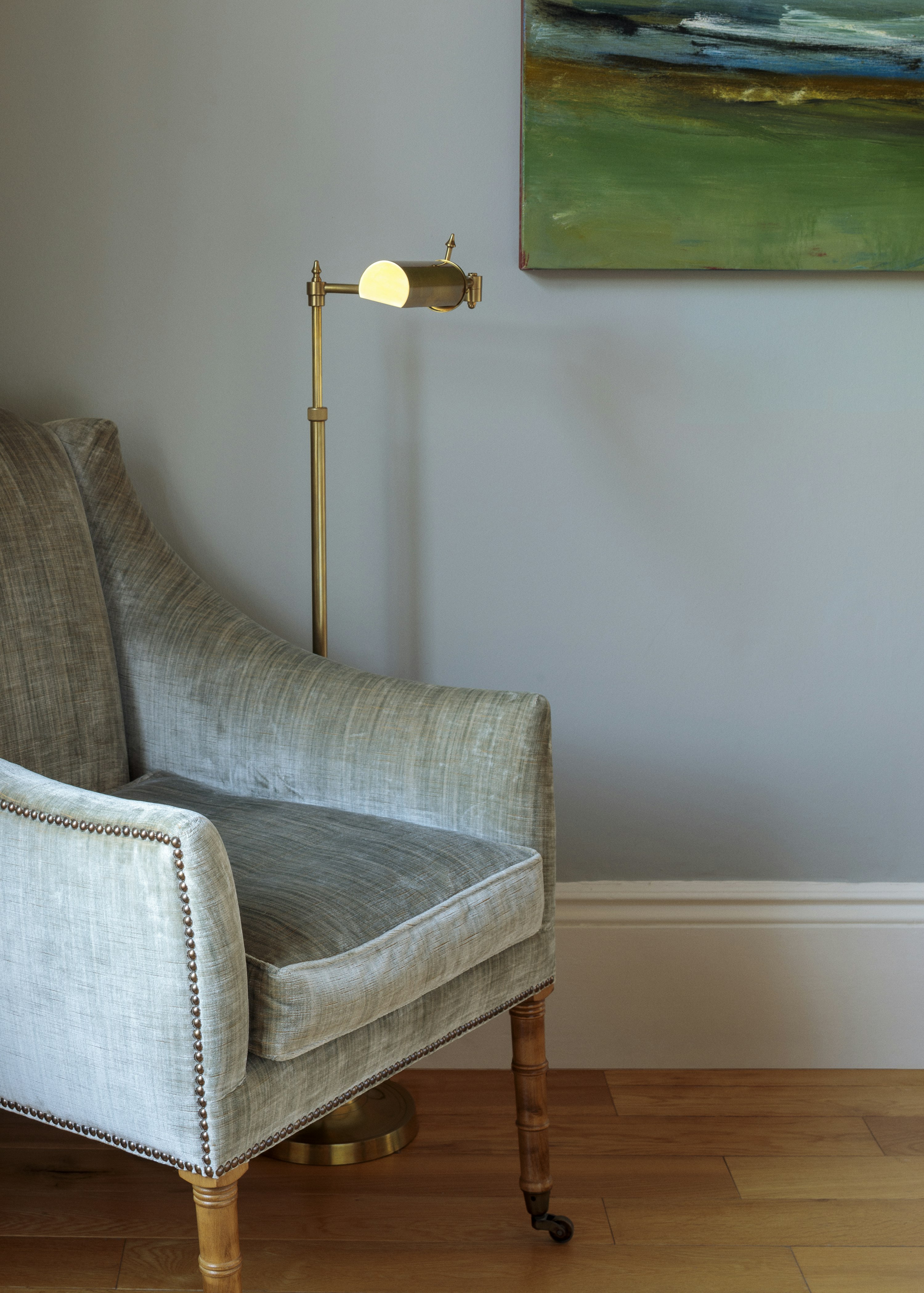 In the corner of the living room, a classic velvet armchair sits next to a brass reading lamp, complementing the warm grey walls.