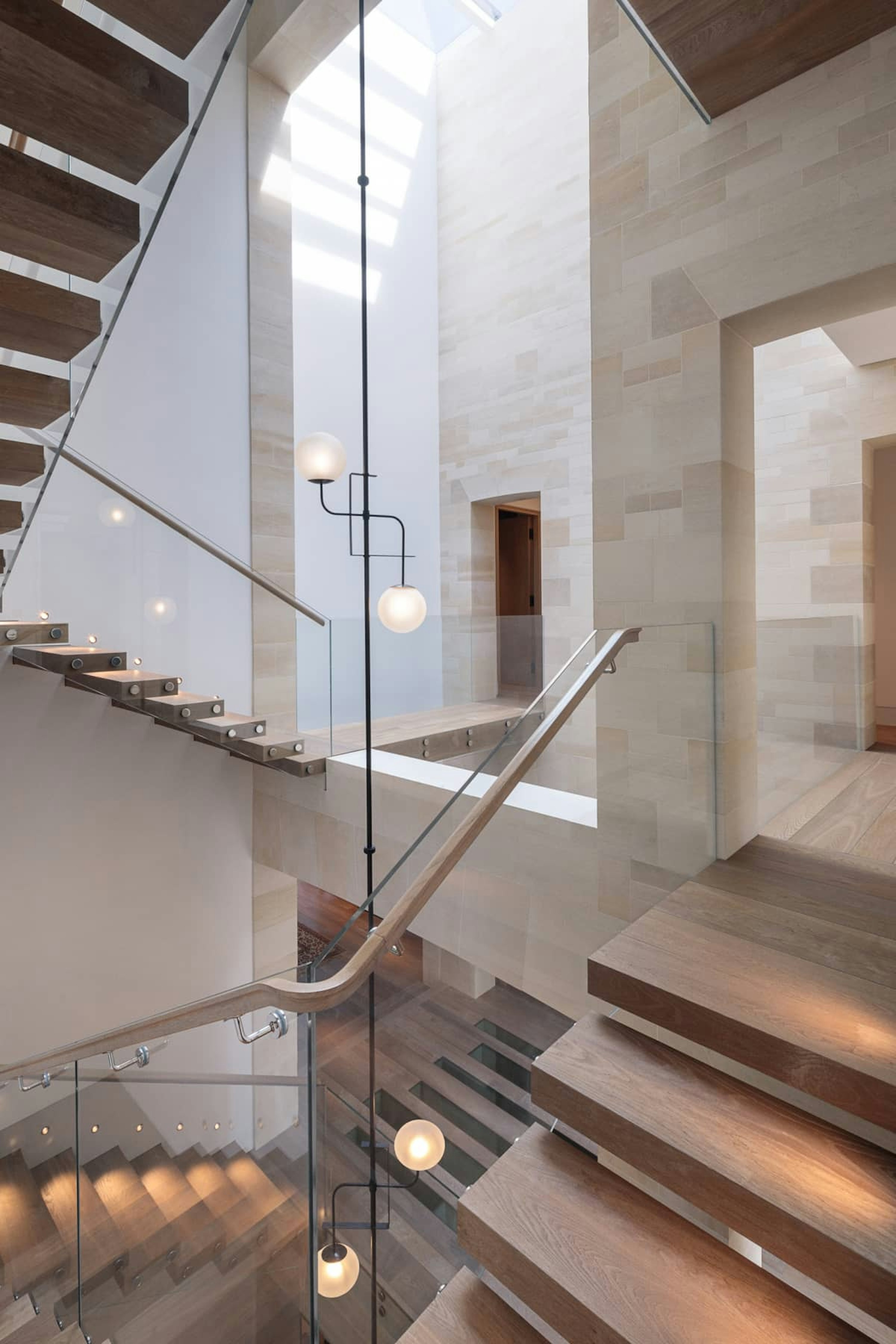 A natural stone, 3-storey stairwell is lit with a skylight and features oak stairs and landings alongside a glass balustrade.