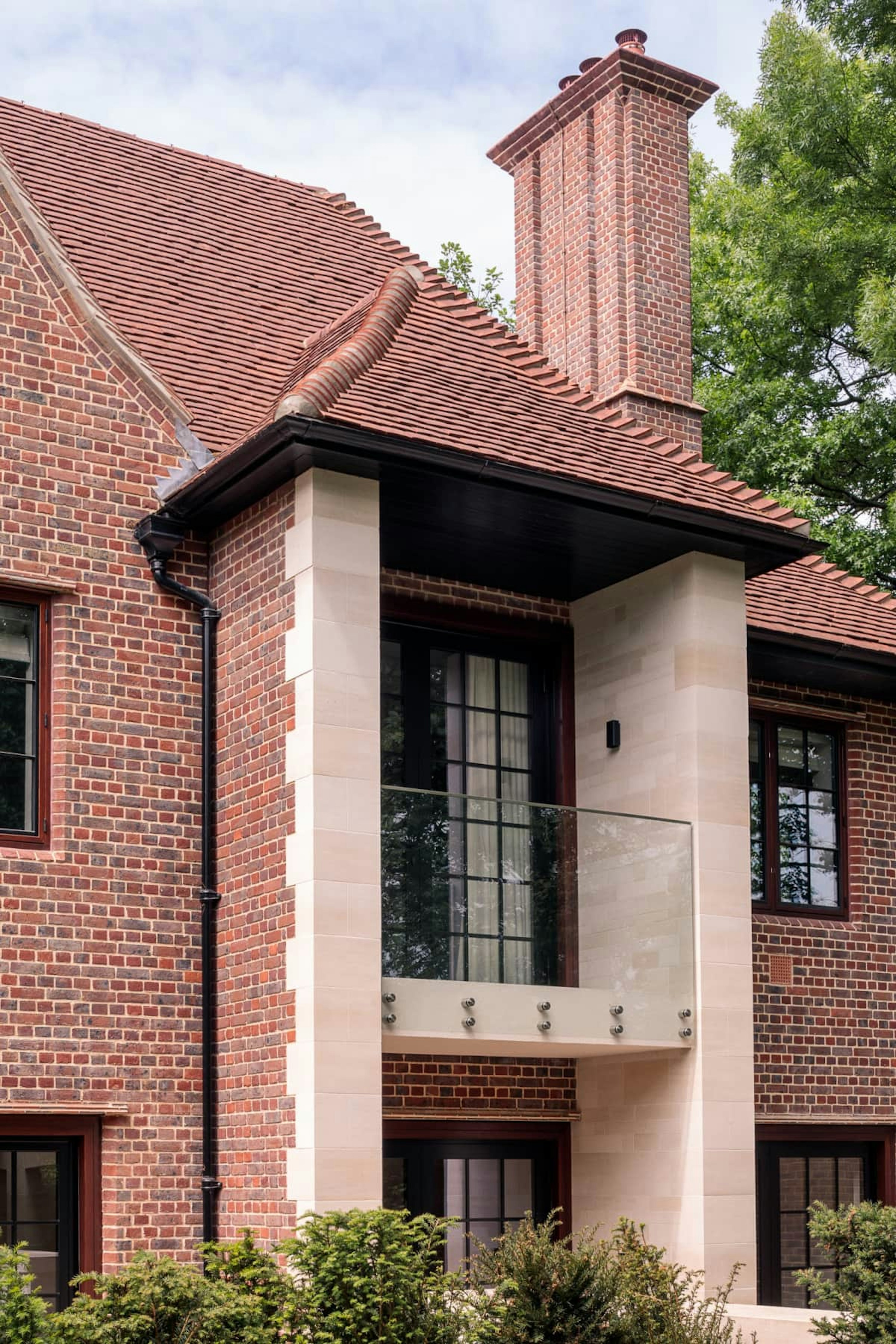 A modern natural stone and red brick home features a sheltered balcony to the master bedroom and overlooks the rear garden.