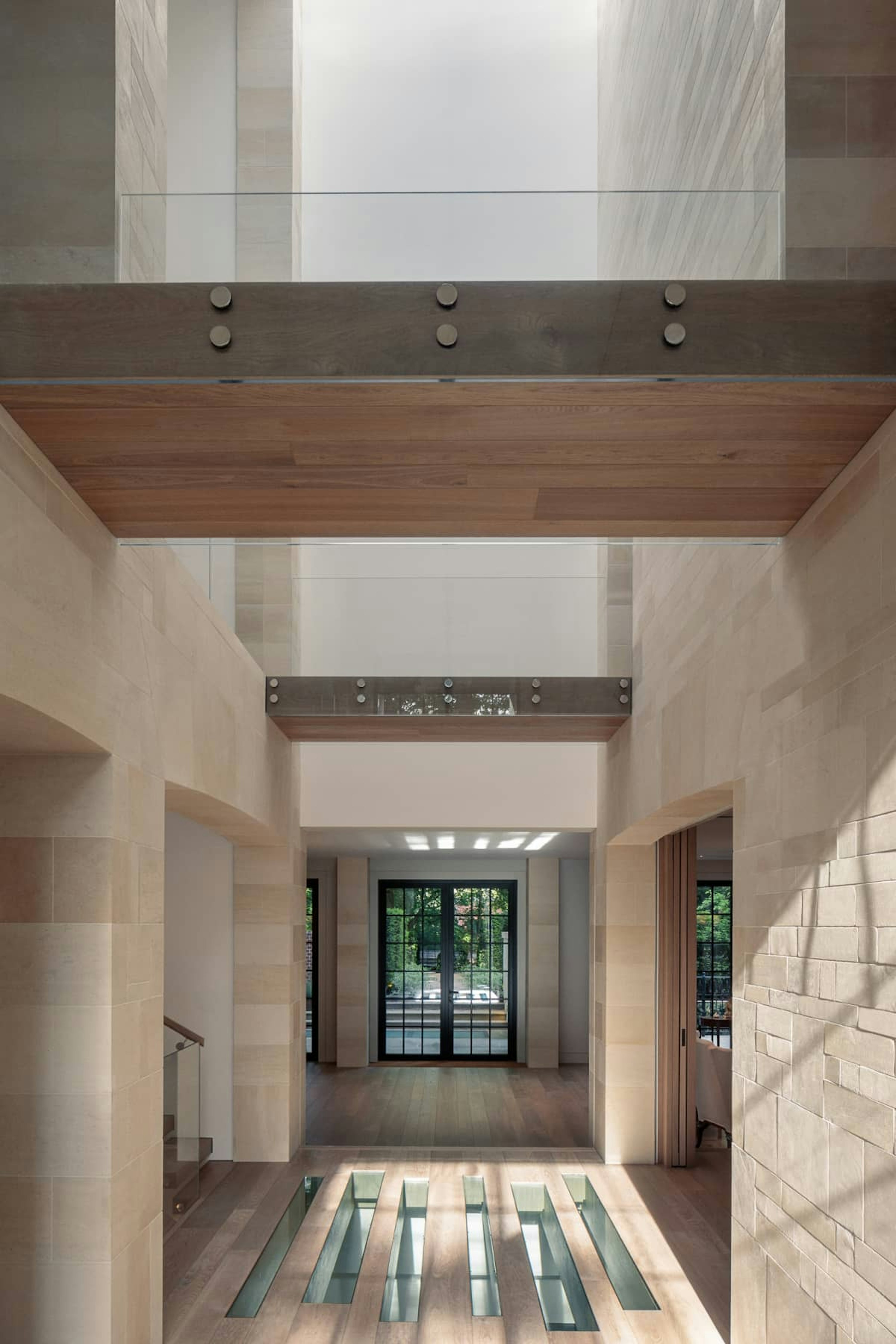 A light, triple-height entryway with pale natural stone walls and glazed floor inlays with doors to the garden.
