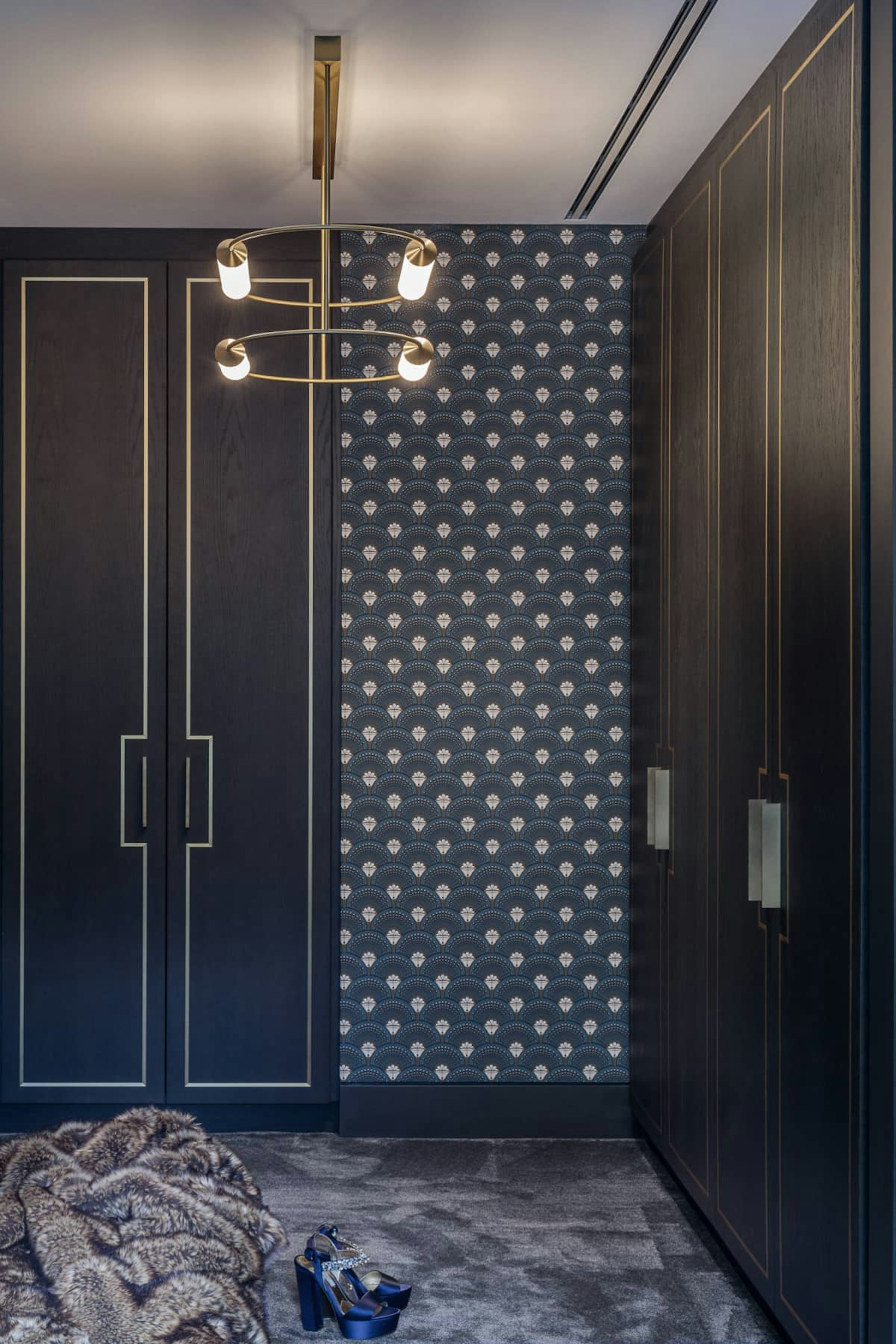 Art Deco style guest bedroom, with dark blue patterned wallpaper. Bespoke wardrobes line the room with a pendant light above.