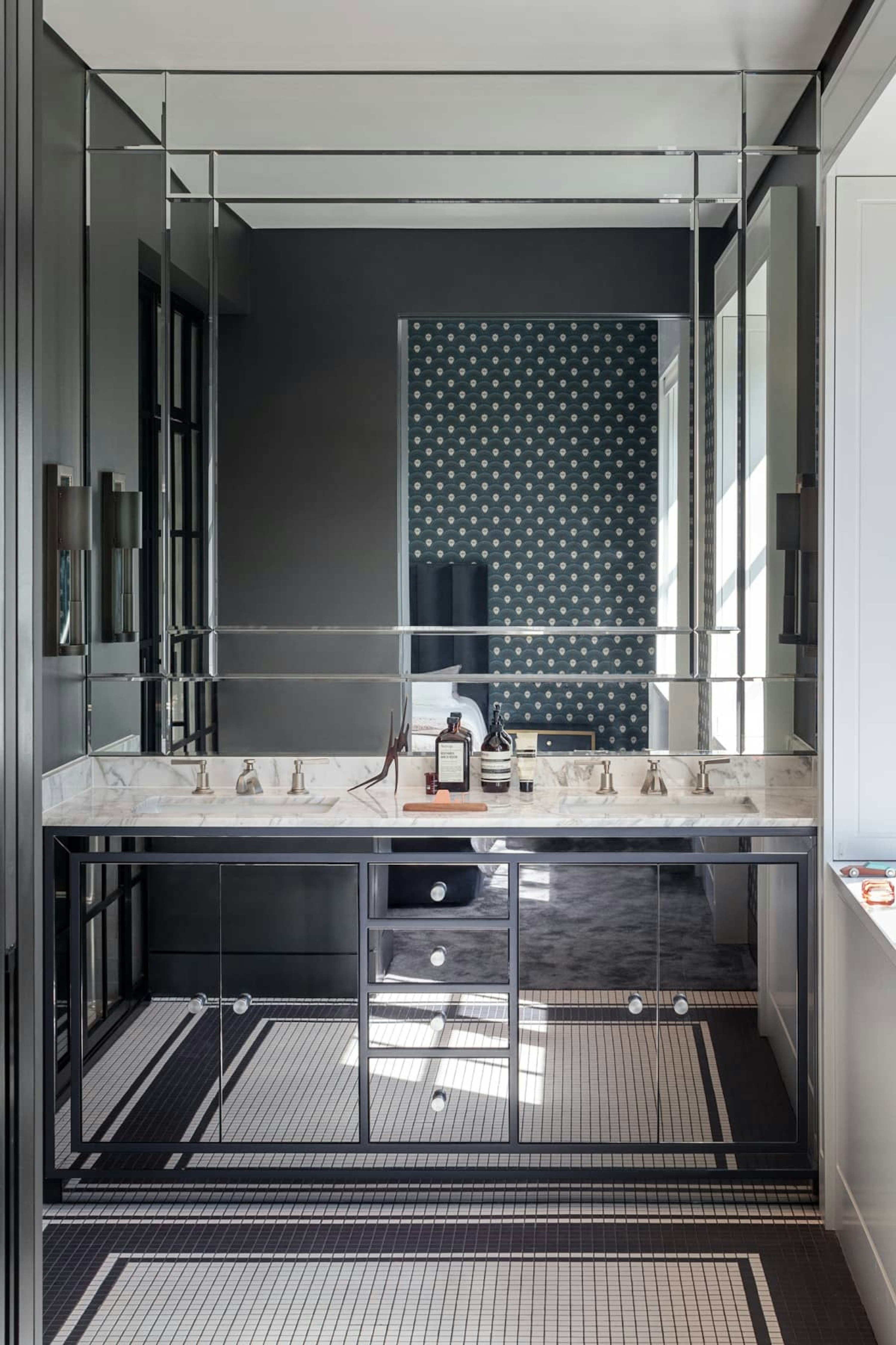 Guest bathroom with a walk-in shower and mirrored cabinets, beneath double sinks with a marble countertop and mosaic flooring.
