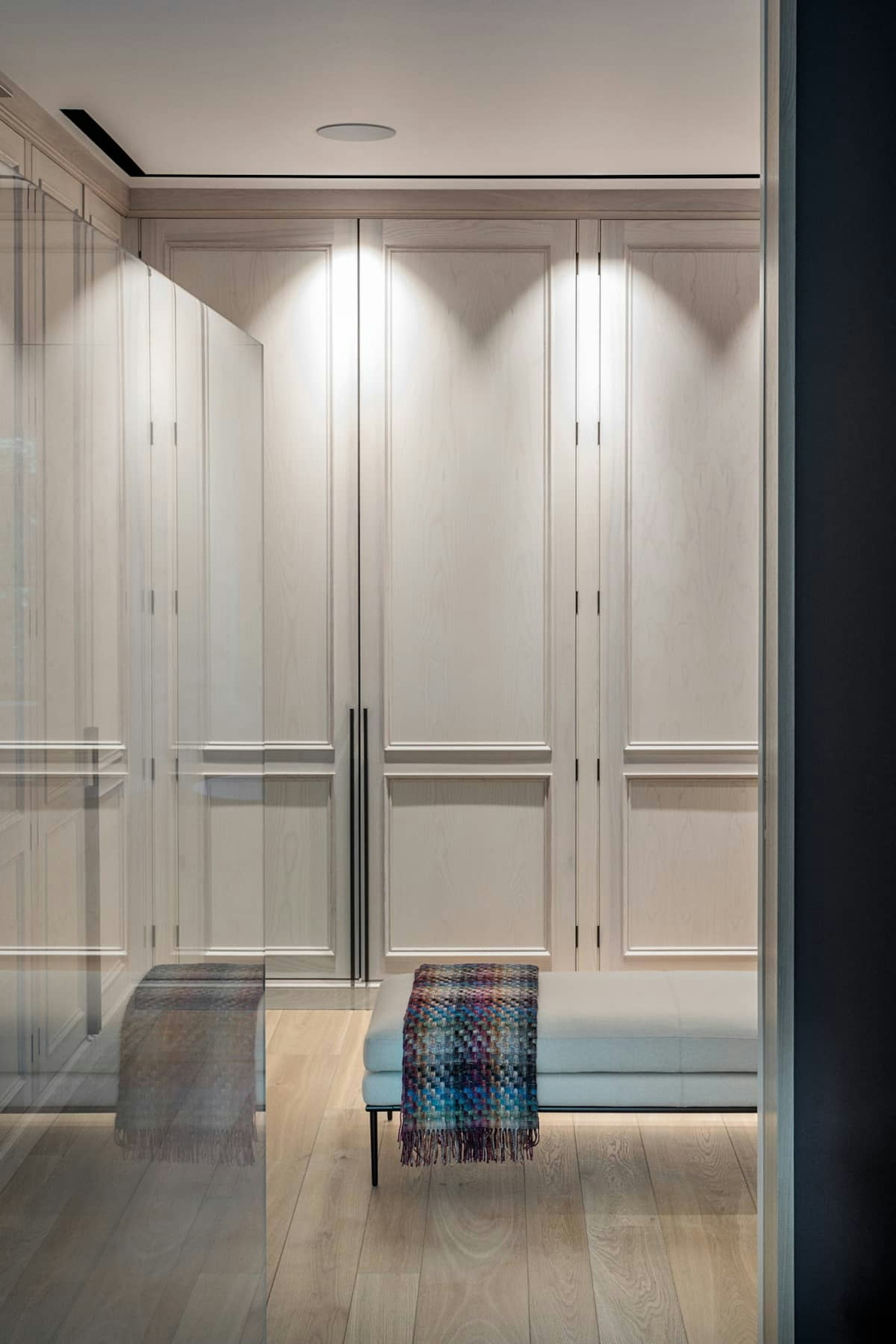 Traditional wardrobe joinery in white-washed timber for a dressing room, with light timber floorboards and a central ottoman.