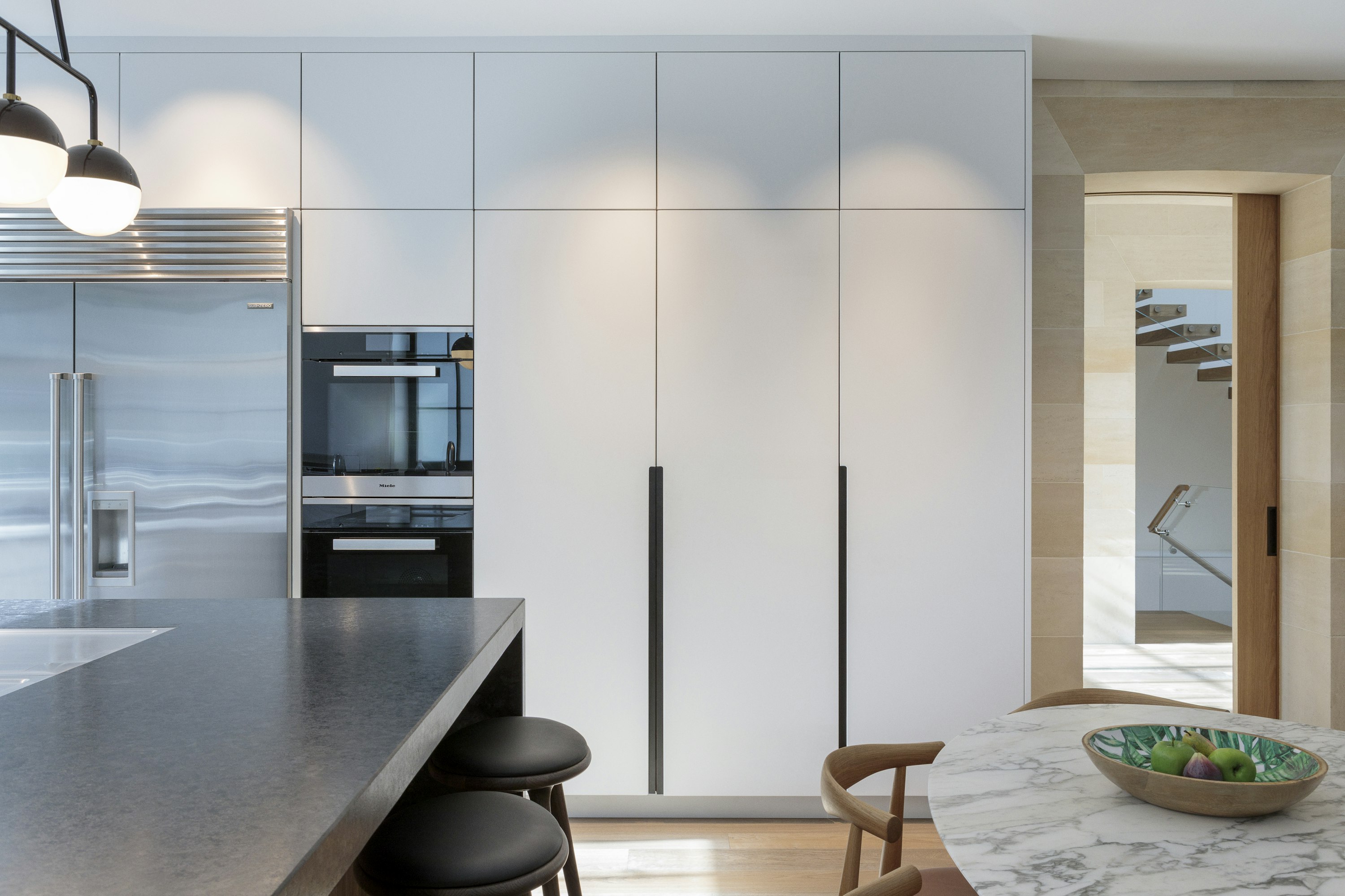 Minimalist, white timber kitchen where floor-to-ceiling cabinets offer lots of storage, next to integrated high-end appliances.
