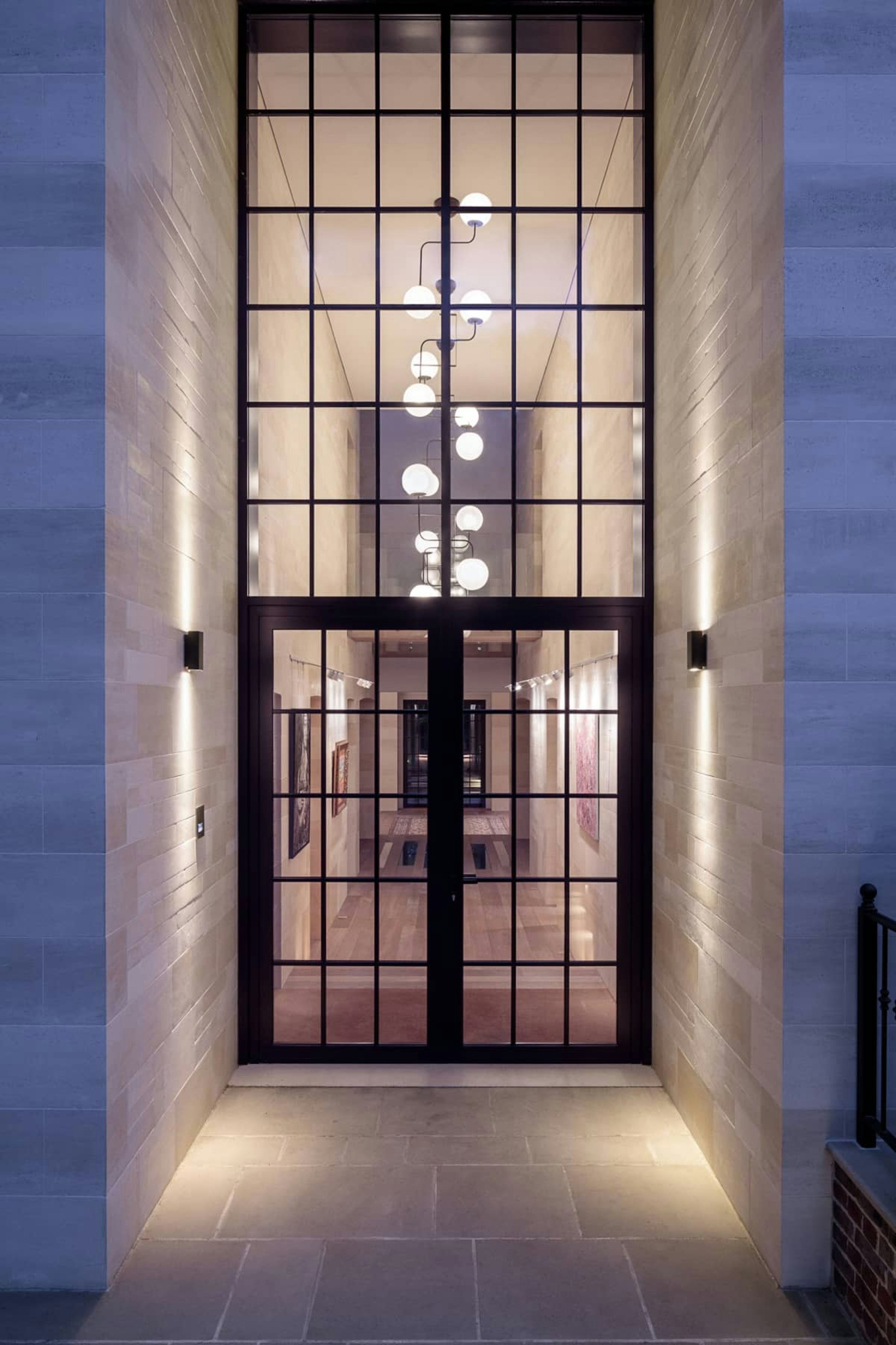Grand, covered entrance and porch into a new home with crittall-style, double front door and natural stone walls.