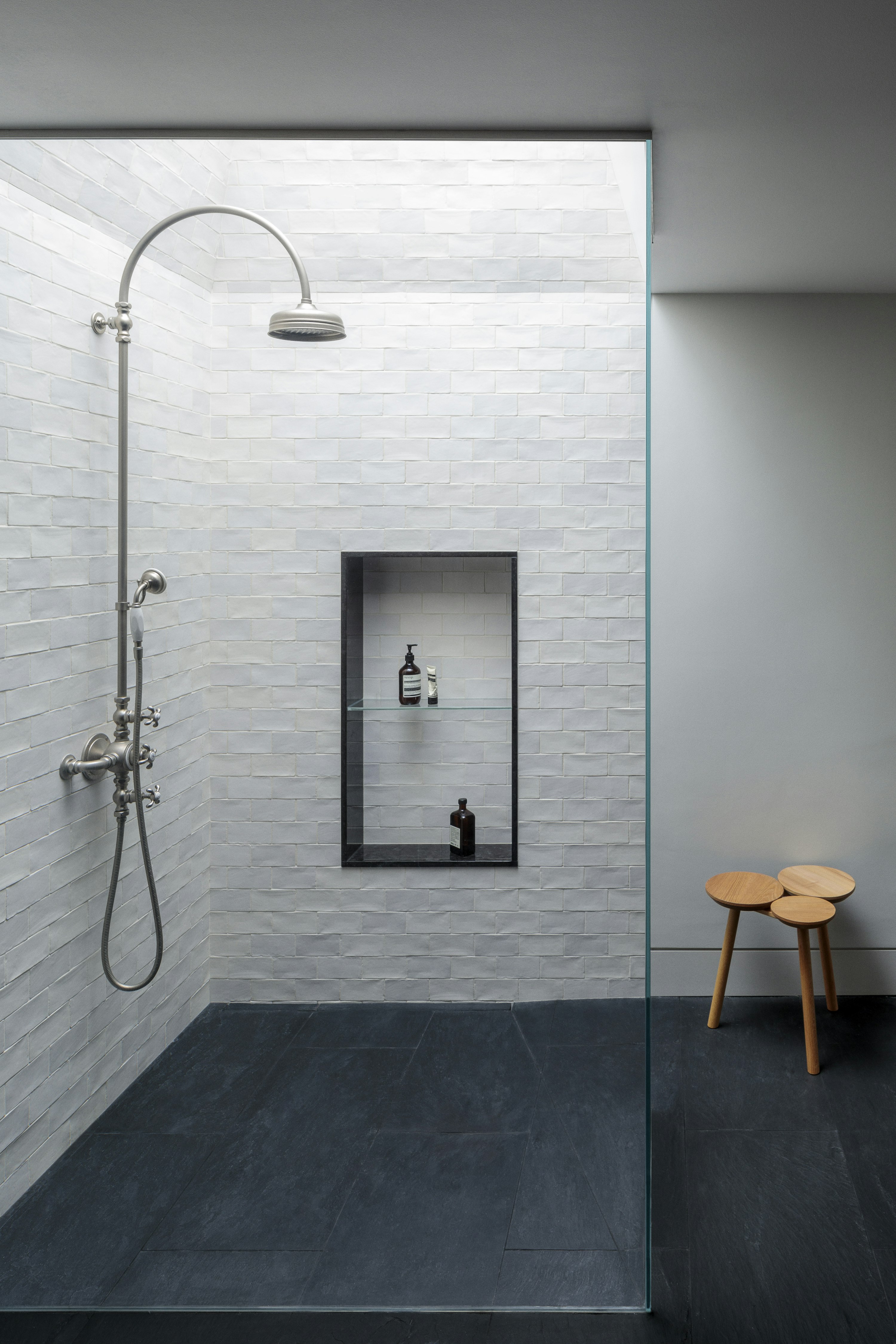 A walk-in shower en-suite features a skylight and a shower niche, with white, hand-made ceramic wall tiles and slate flooring.