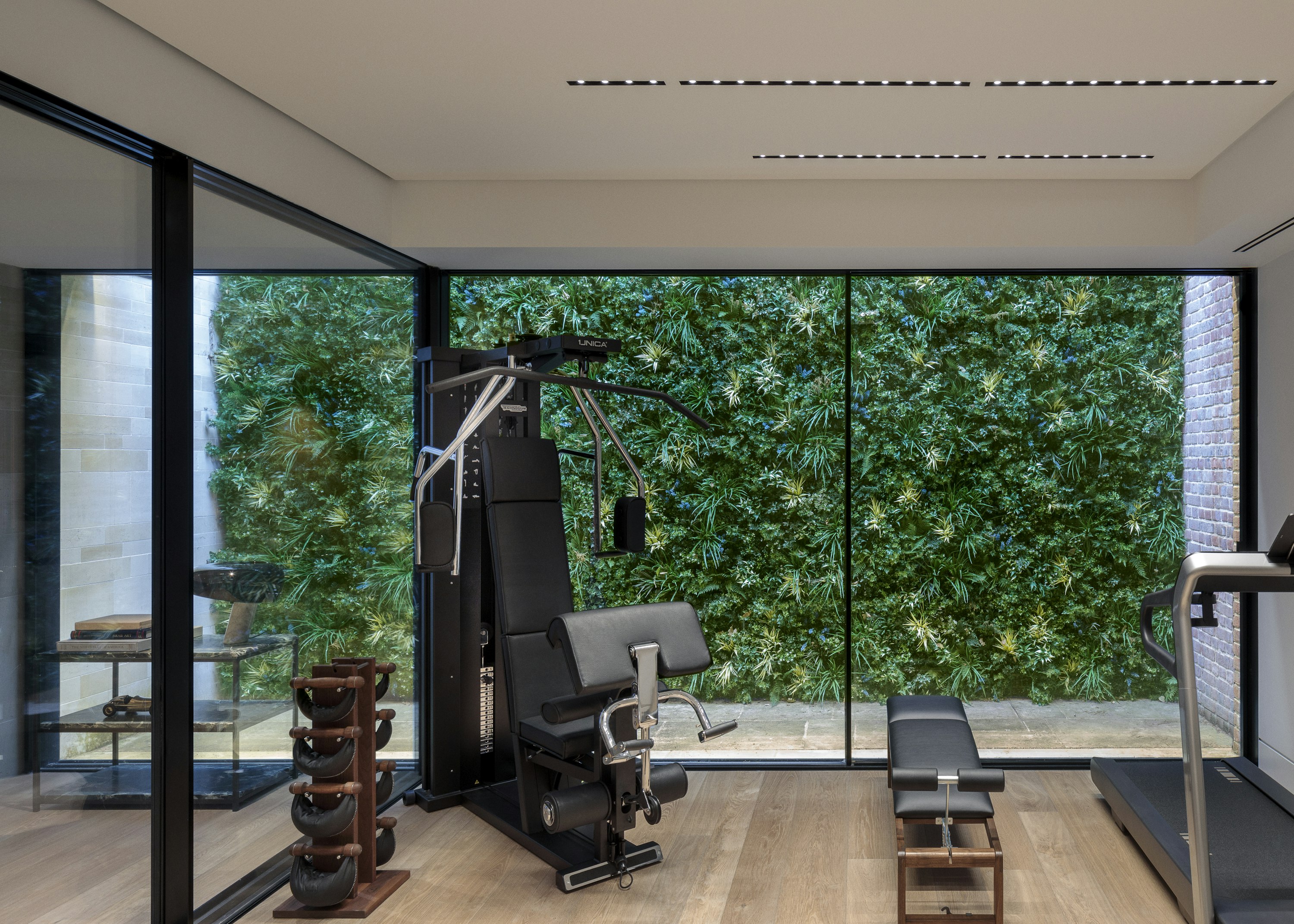 A state-of-the-art home gym with weight-lifting equipment and views onto a large lightwell with an artificial green wall.