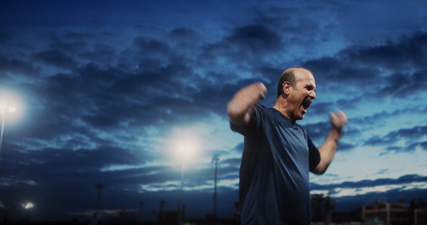 Man celebrating at a football pitch illuminated by a floodlight