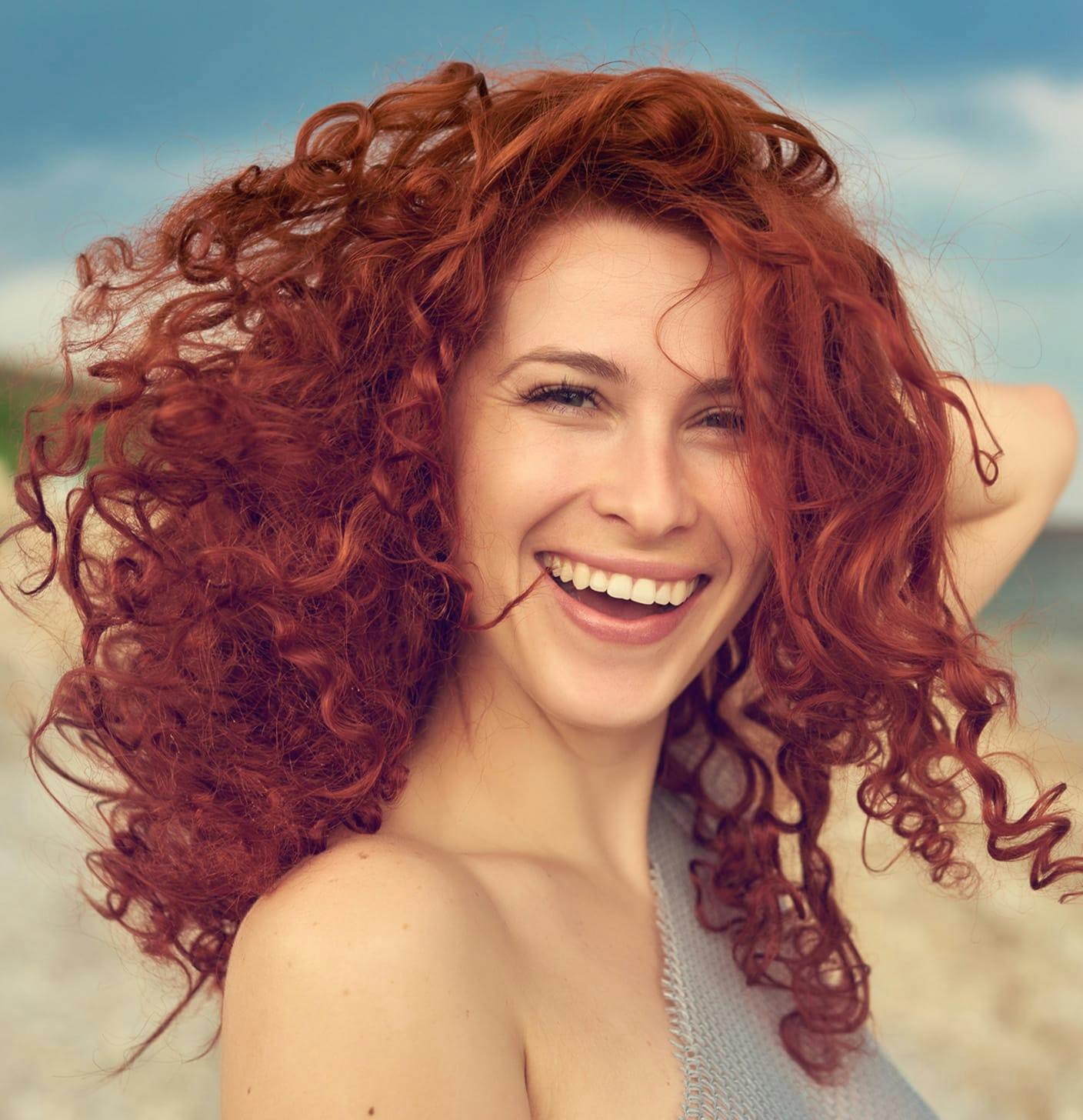 Woman with curly red hair smiling on the beach